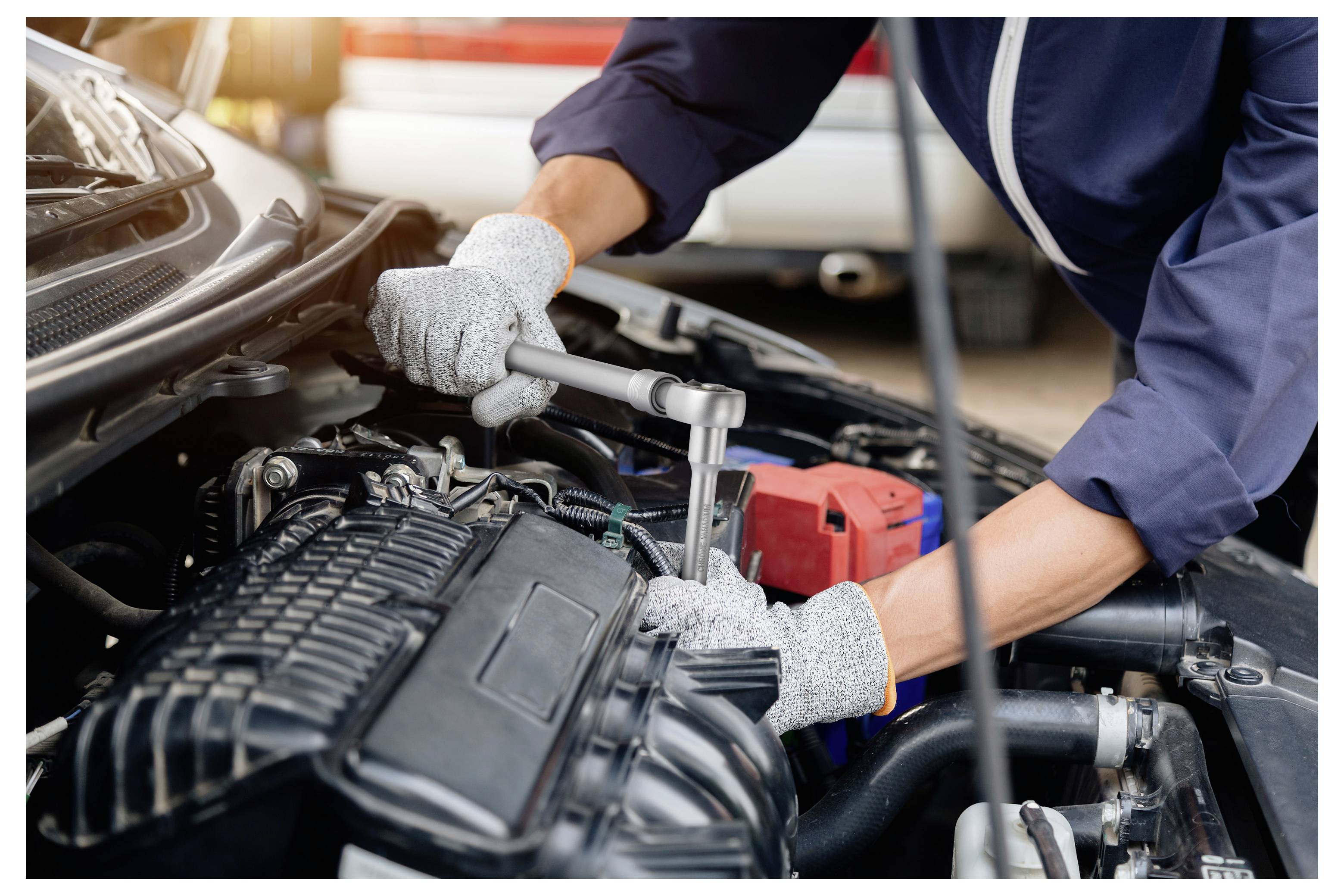 Mechaniker mit einem Schraubenschlüssel, der einen Automotor unter offener Motorhaube wartet, wobei die Batterie und Motorkomponenten sichtbar sind.