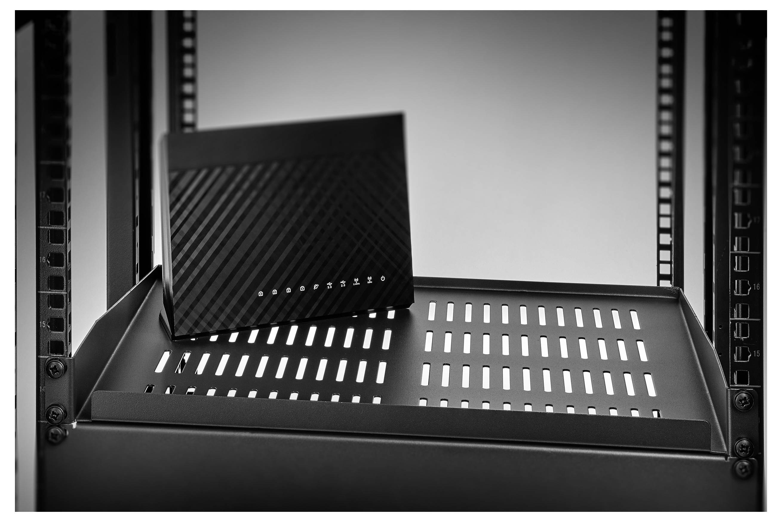 Schwarzer Netzwerk-Router oder Modem auf einem Serverrack-Regal mit vorderen Anzeigelichtern und diagonaler Textur.