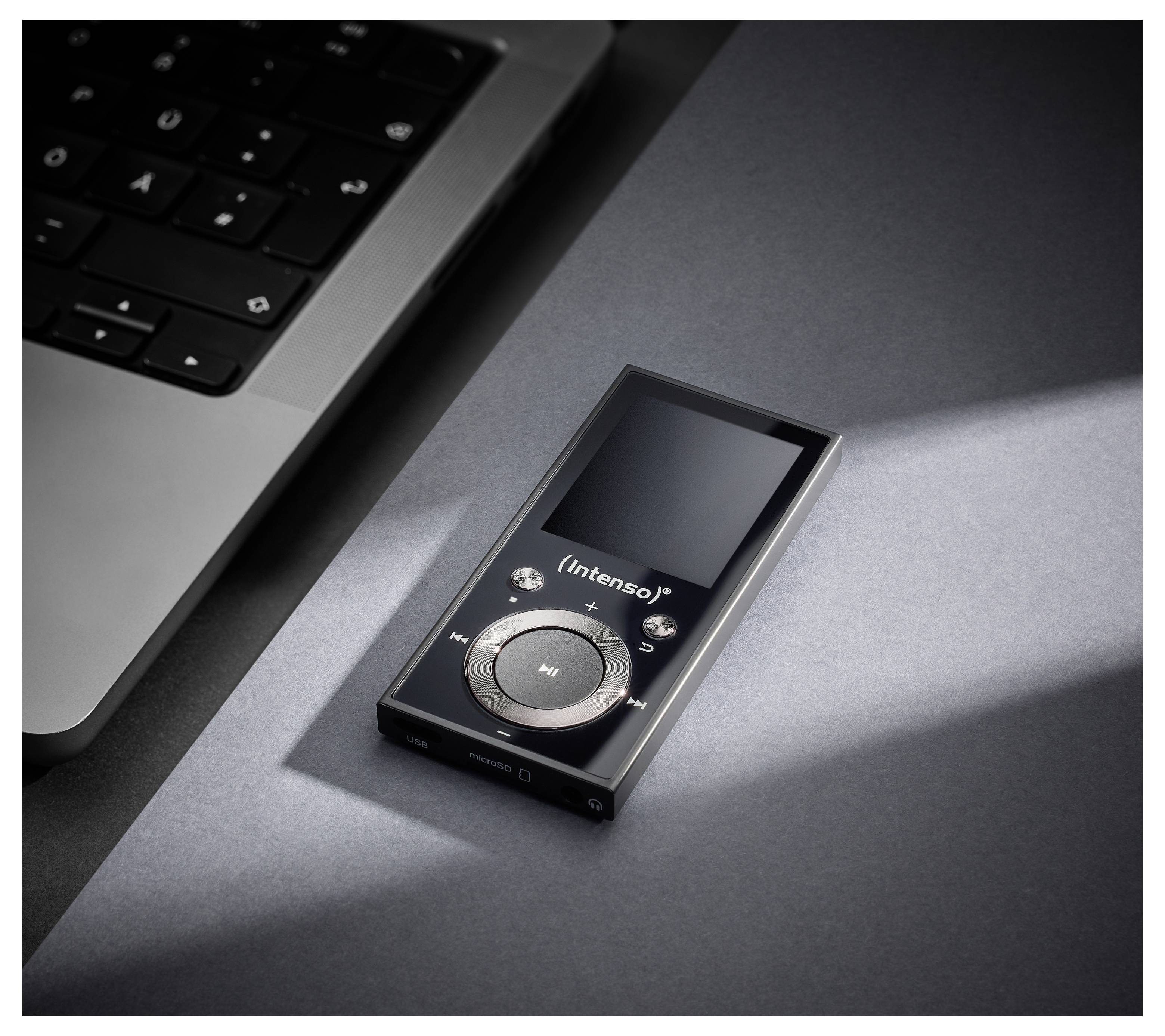 Ein schwarzer Intenso MP3-Player mit einem kreisförmigen Steuerpad ruht auf einer grauen Oberfläche in der Nähe einer Laptop-Tastatur, beleuchtet von einem Lichtstrahl.