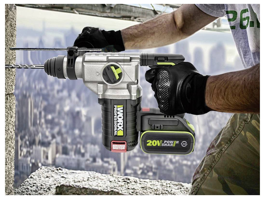 Eine Person benutzt einen Worx 20V Elektrobohrer, um ein Loch in eine Betonwand zu bohren, trägt Handschuhe und steht auf einer Baustelle eines Hochhauses.