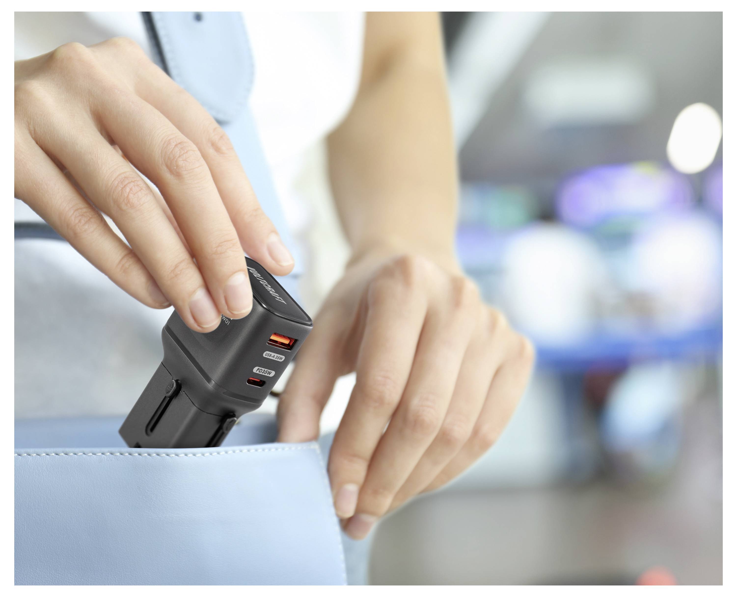 Eine Person legt einen kompakten schwarzen Mehrfach-Stromadapter mit USB-Anschlüssen in eine hellblaue Handtasche, was Tragbarkeit und Komfort suggeriert.