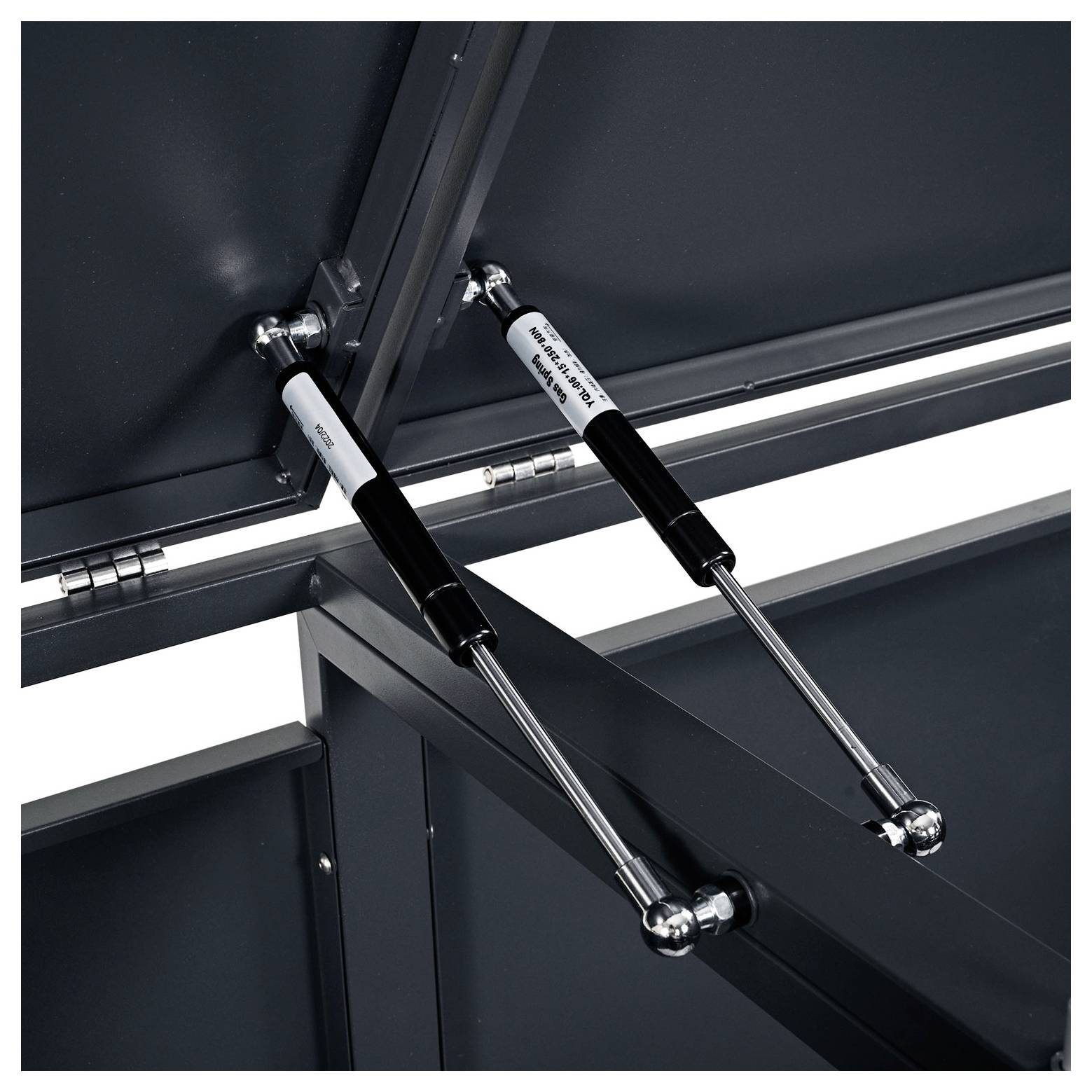 Zwei metallene Scharnierstützen mit hydraulischen Streben, die Teile eines dunklen Rahmens verbinden, möglicherweise zum Öffnen oder Stabilisieren eines Deckels oder Panels.