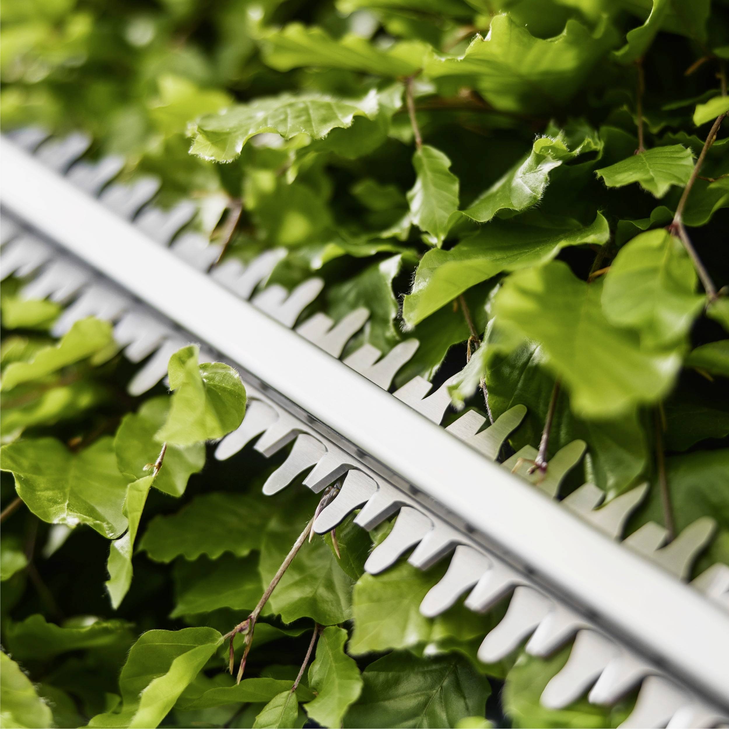 Ein Heckenschneider, der durch lebhaft grüne Blätter eines Busches schneidet und dabei sauber geschnittenes Laub und scharfe, silberne Klingen in Aktion zeigt.