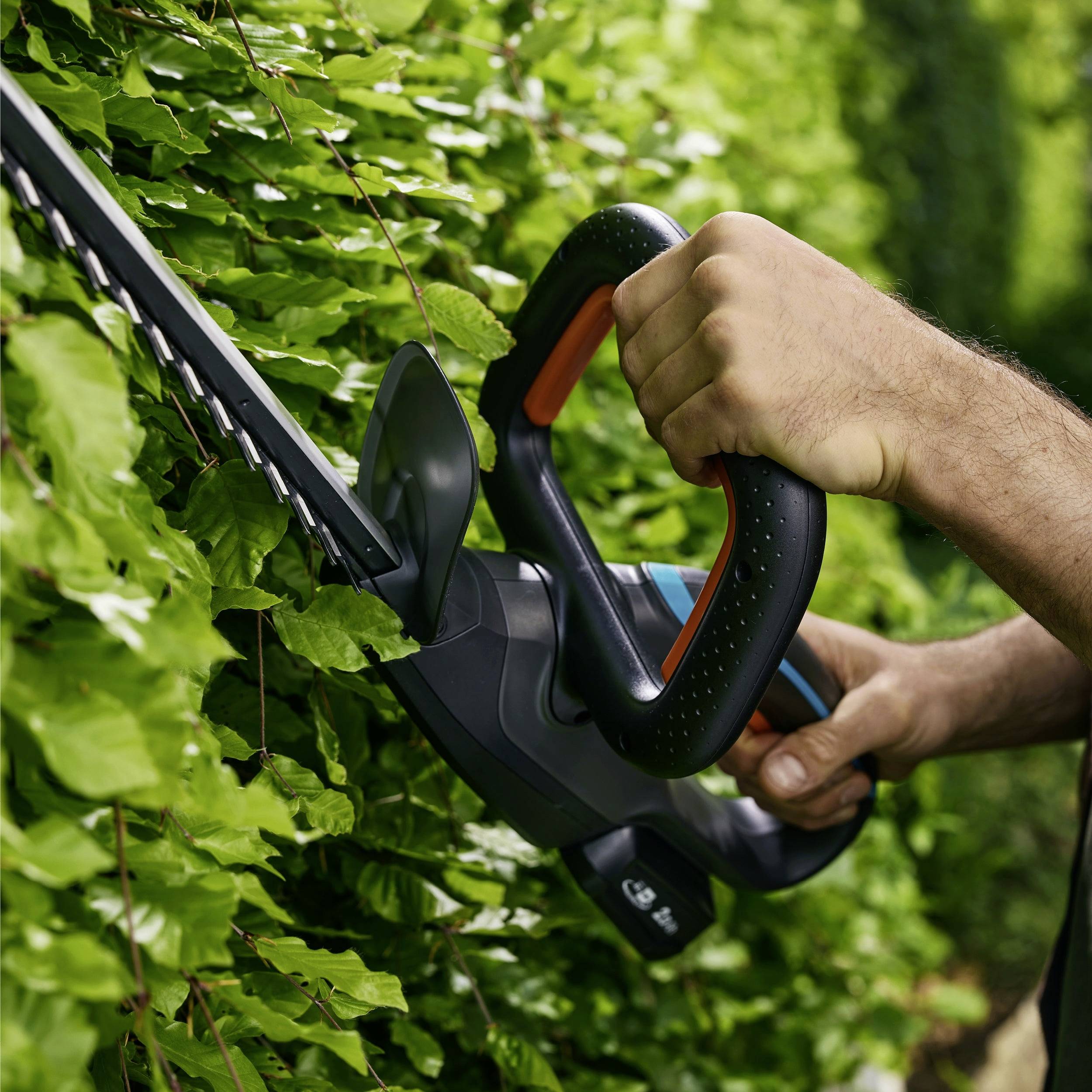 Eine Person schneidet eine Hecke mit einem elektrischen Heckenschneider, was die Gartenpflege veranschaulicht.