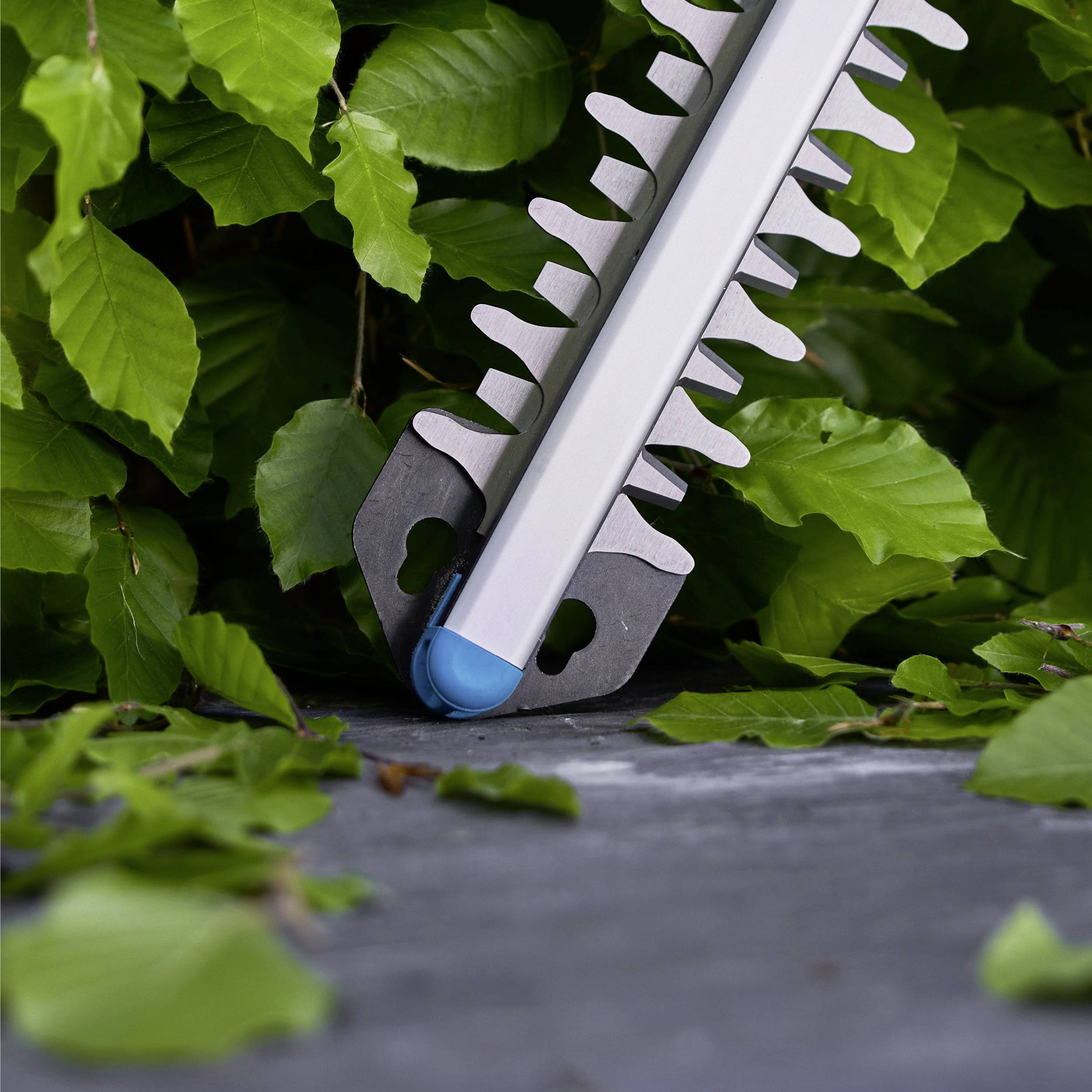 Ein Heckenschneider, der auf einer Betonoberfläche ruht, ist von üppig grünen Blättern umgeben und deutet auf Gartenarbeit oder Landschaftsgestaltung hin.