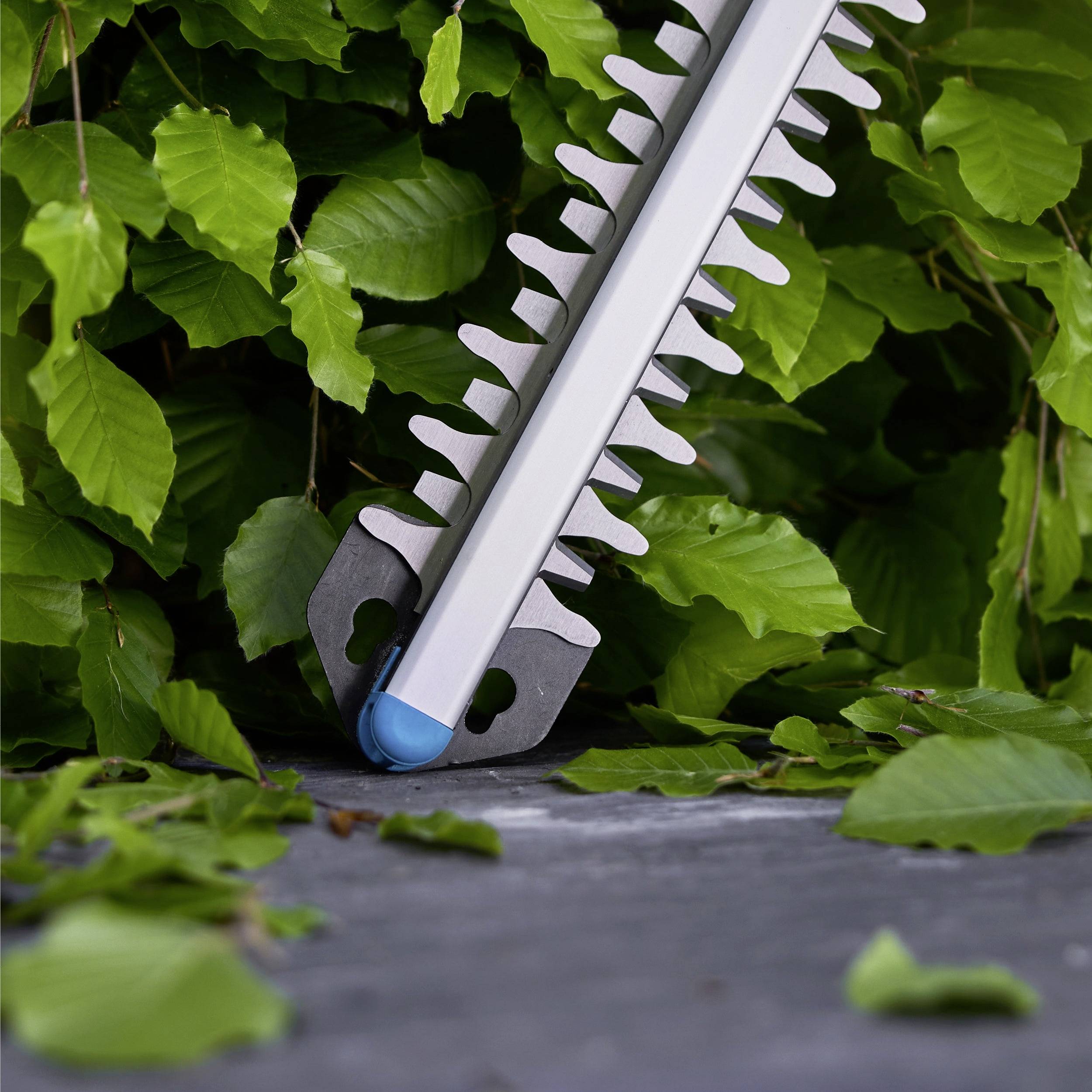 Eine Heckenscherklinge mit scharfen Zähnen, die zwischen grünen Blättern positioniert ist und darauf hindeutet, dass sie zum Schneiden oder Formen von Hecken entwickelt wurde.