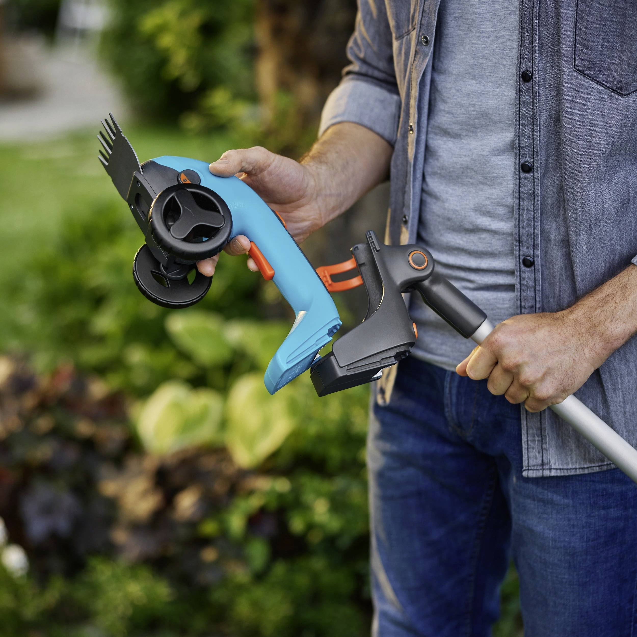 Eine Person in einem blauen Hemd hält ein Gartenwerkzeug und beschneidet Pflanzen in einer Gartenumgebung. Üppiges, grünes Blattwerk ist im Hintergrund sichtbar.