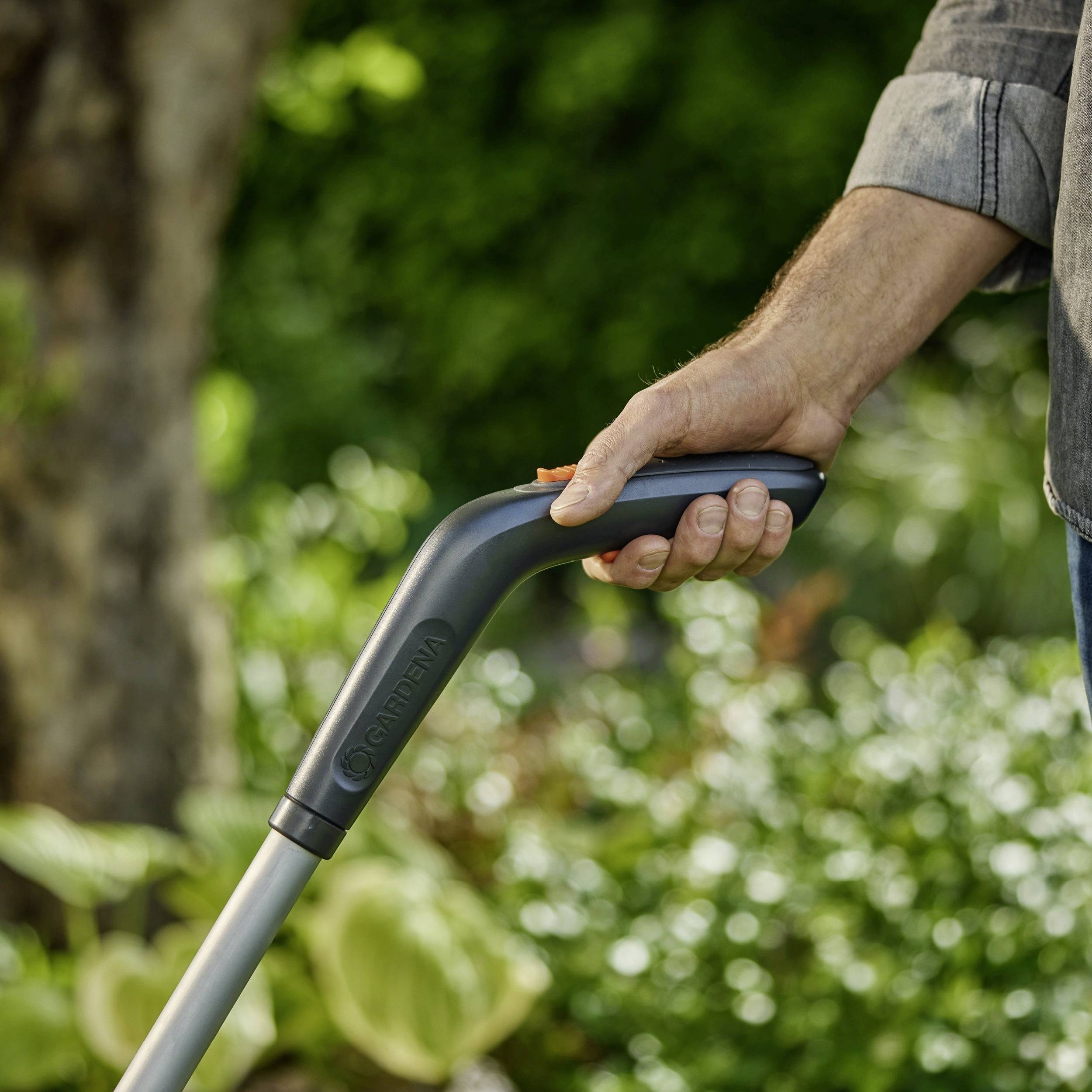 Eine Hand, die den Griff eines Gartengeräts im Freien hält, mit unscharfem Grün im Hintergrund.