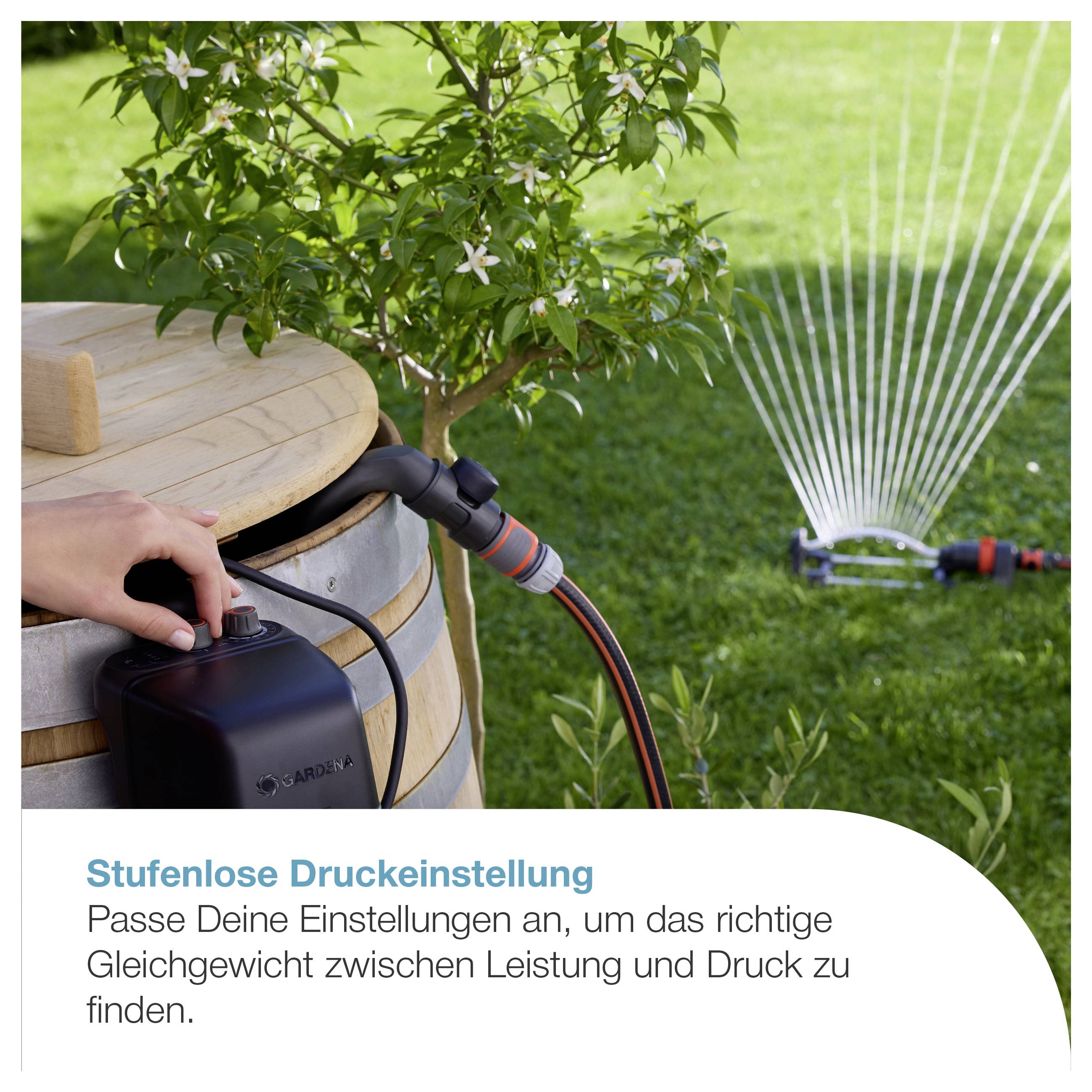 Person stellt an einem Gartenschlauchsystem die stufenlose Druckeinstellung ein; Sprinkler bewässert den Rasen im Hintergrund.