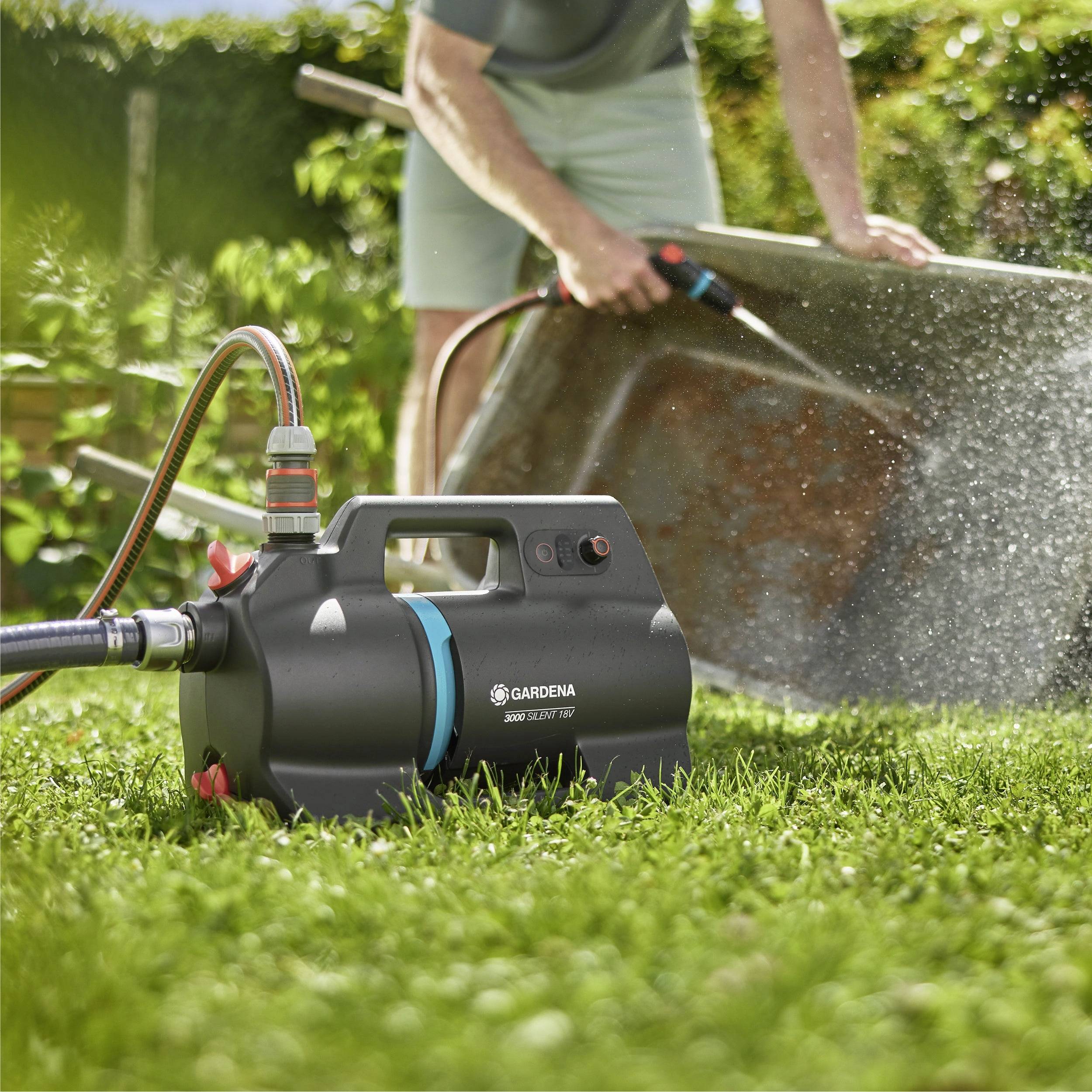 Eine Person verwendet eine Gartenwasserpumpe, um eine große Metalloberfläche in einem sonnigen Garten zu reinigen und demonstriert damit die Vielseitigkeit der Pumpe bei Reinigungsaufgaben.