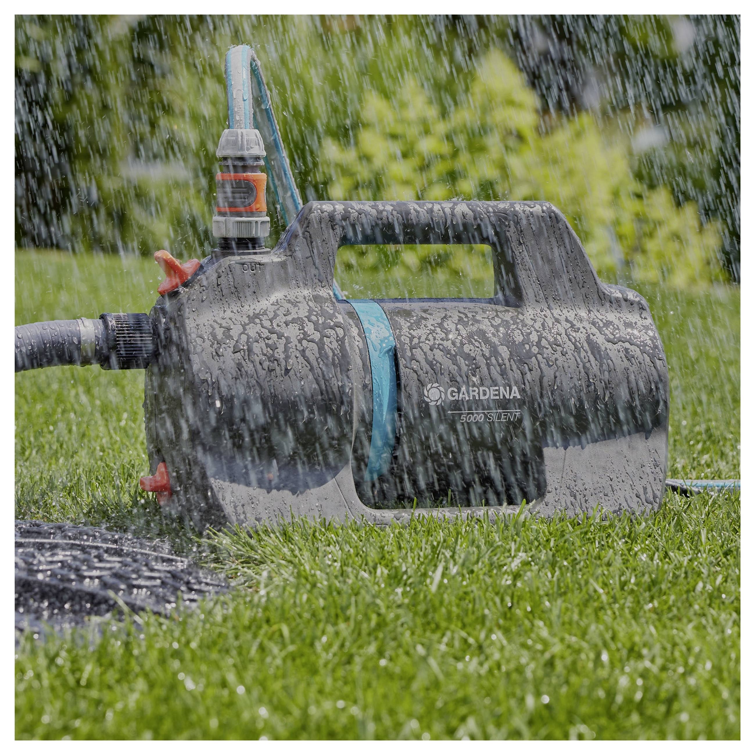 Eine Gardena-Wasserpumpe, die auf einem Rasen unter starkem Regen betrieben wird, mit sichtbaren Wassertropfen auf der Ausrüstung und dem Gras.