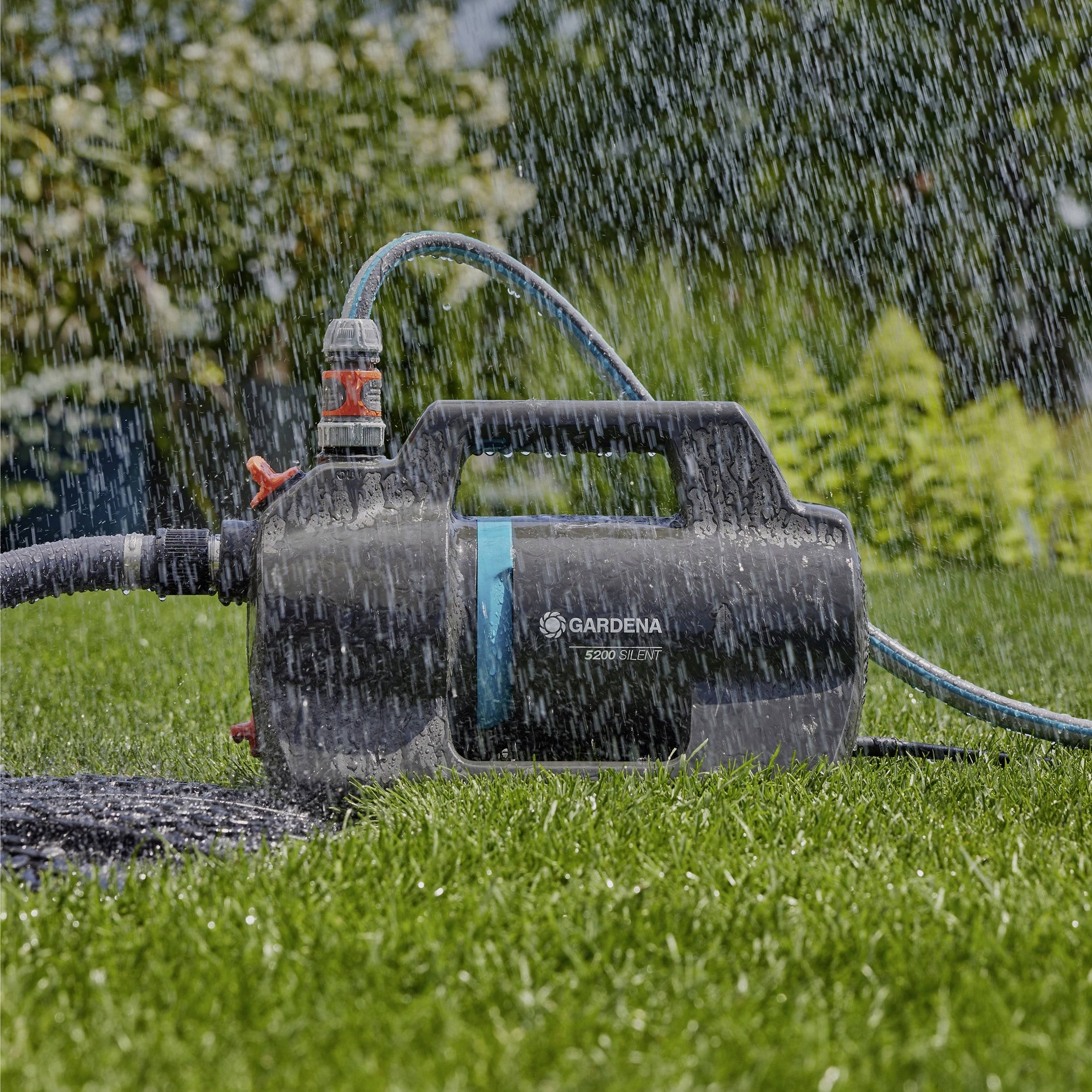 Ein Gartenschlauch-Sprinklersystem bewässert einen grünen Rasen, wobei eine schwarze und blaue Zentrale mit der Aufschrift „Gardena