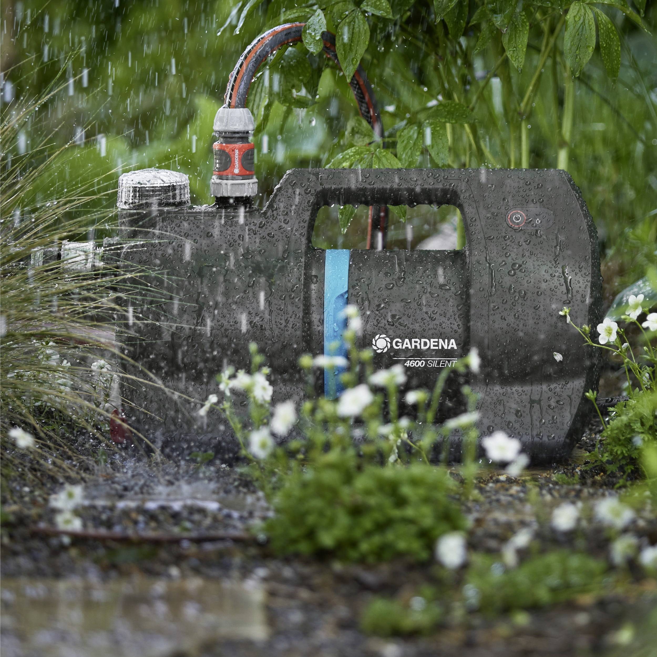 Tragbare Wasserpumpe in einer regnerischen Gartenumgebung, umgeben von Pflanzen, die den Wasserfluss effizient durch einen Auslauf und einen angeschlossenen Schlauch umleitet.