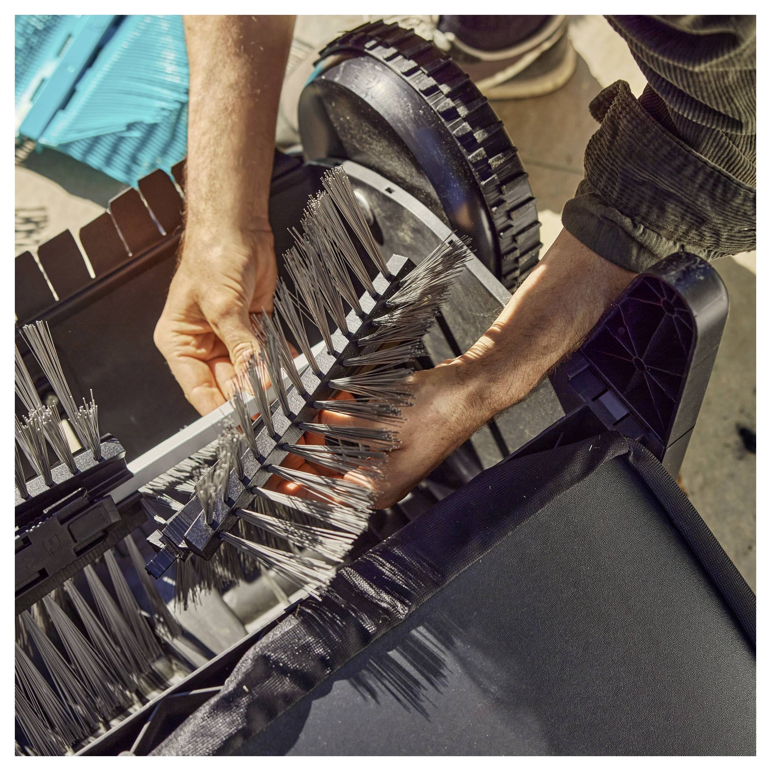 Hände montieren oder passen einen zylindrischen Bessenschaft an, der an einer Maschine mit Rädern befestigt ist, draußen an einem sonnigen Tag.