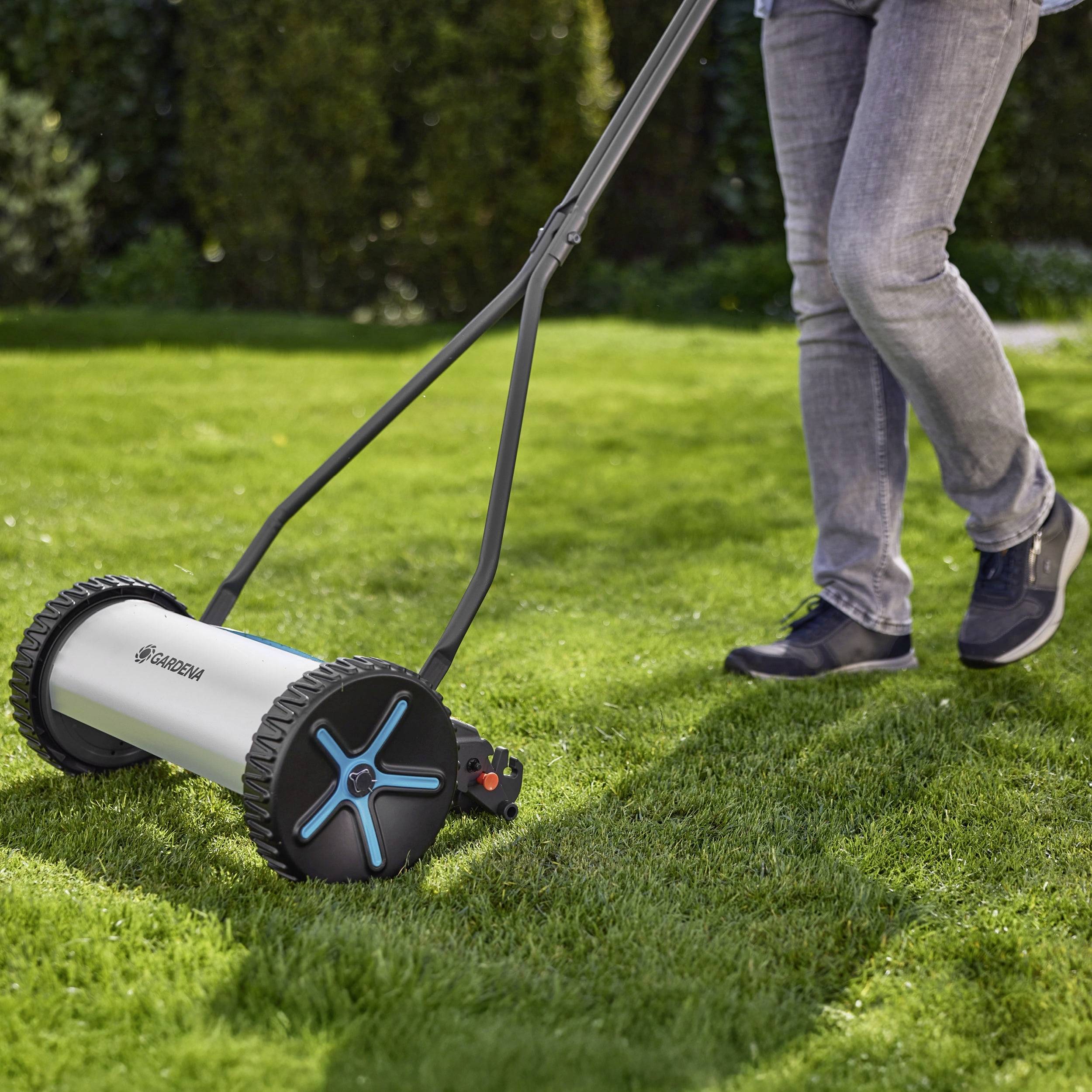 Eine Person, die an einem sonnigen Tag einen Rasen mit einem manuellen Rasenmäher mäht und dabei umweltfreundliche Gartenpraktiken hervorhebt.