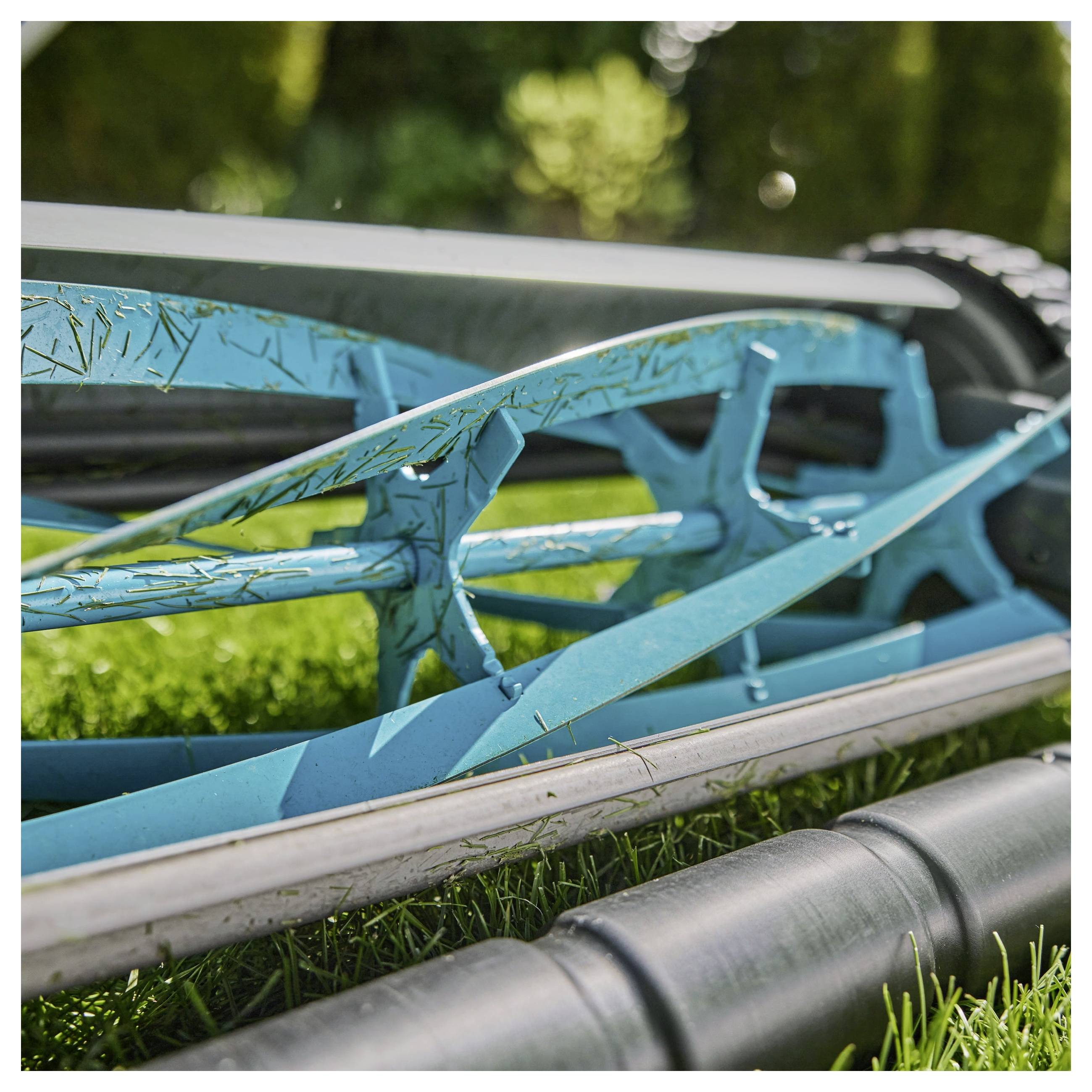 Eine Nahaufnahme eines manuellen Spindelmähers mit blauen Metallwalzen, die Gras schneiden, mit Betonung der mechanischen Klingen und des Mäherdesigns.