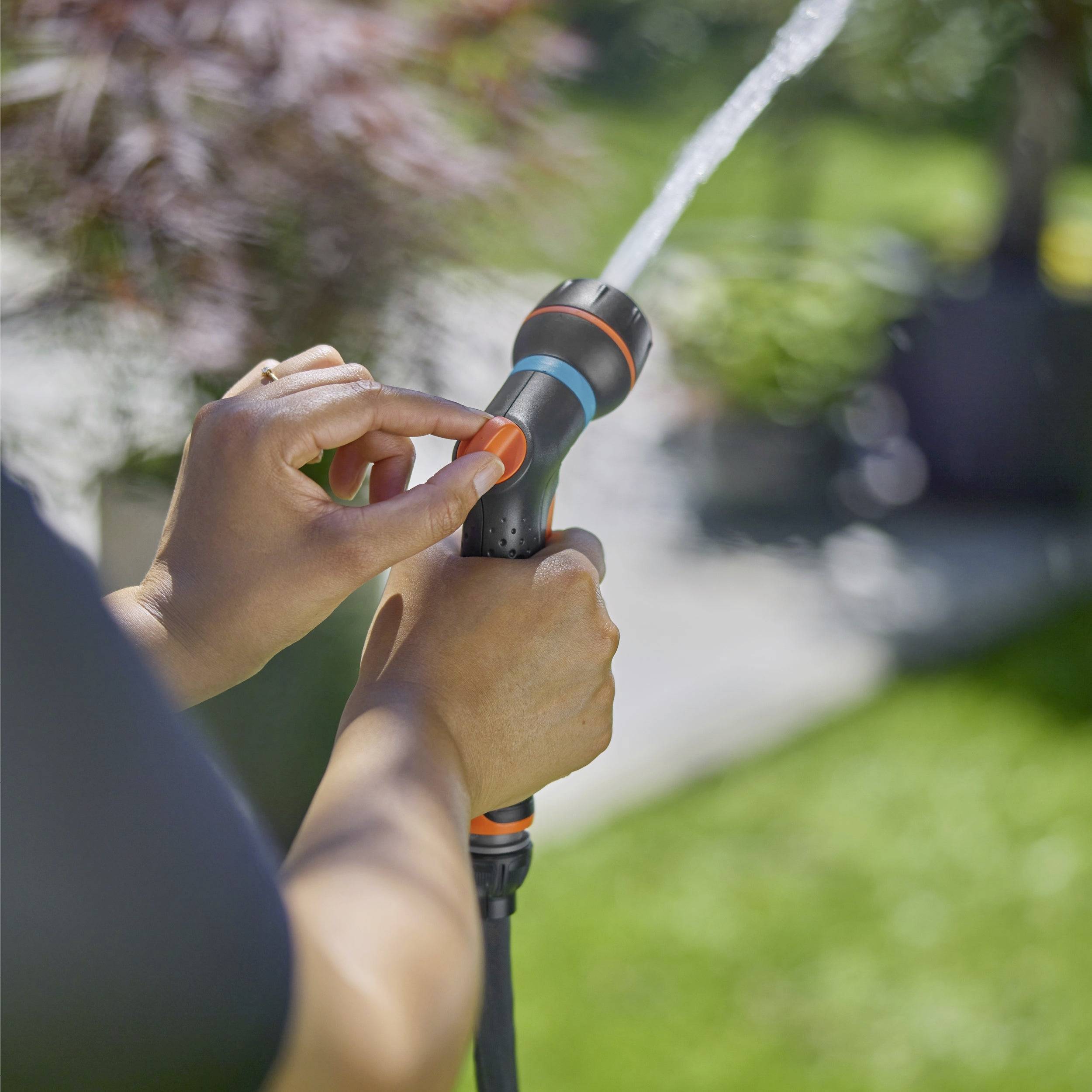 Eine Person stellt die Düse eines Gartenschlauchs ein und spritzt Wasser auf einen Rasen.