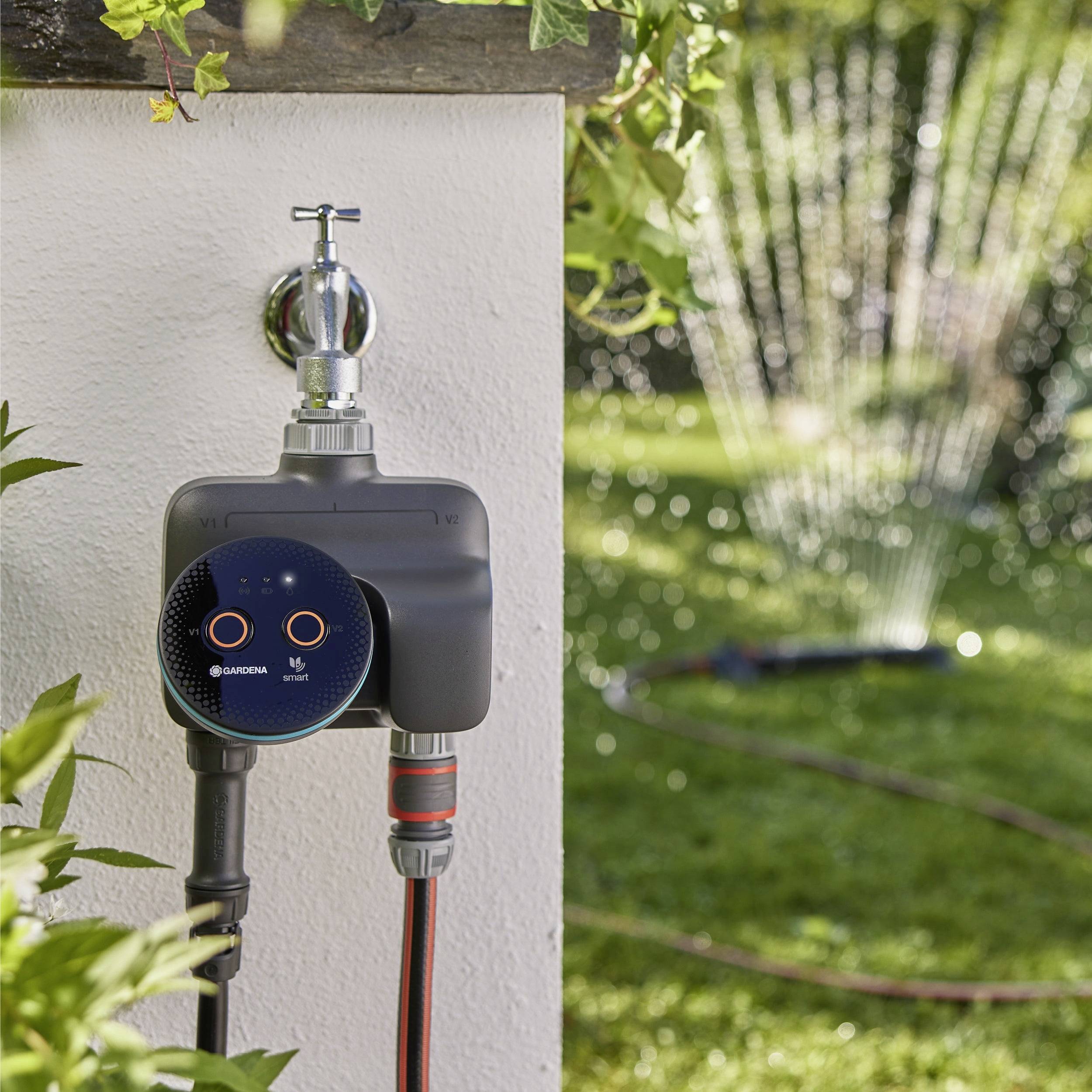 Ein digitaler Wasserzeitschalter ist an einem Außenwasserhahn befestigt, der einen Schlauch steuert, der einen Garten mit einem oszillierenden Sprinkler bewässert.