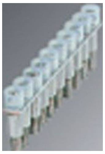 Eine Reihe von neun hellblauen zylindrischen Objekten, die an Stiften auf einer metallischen Oberfläche angebracht sind, möglicherweise ein Stecker oder eine elektronische Komponente.