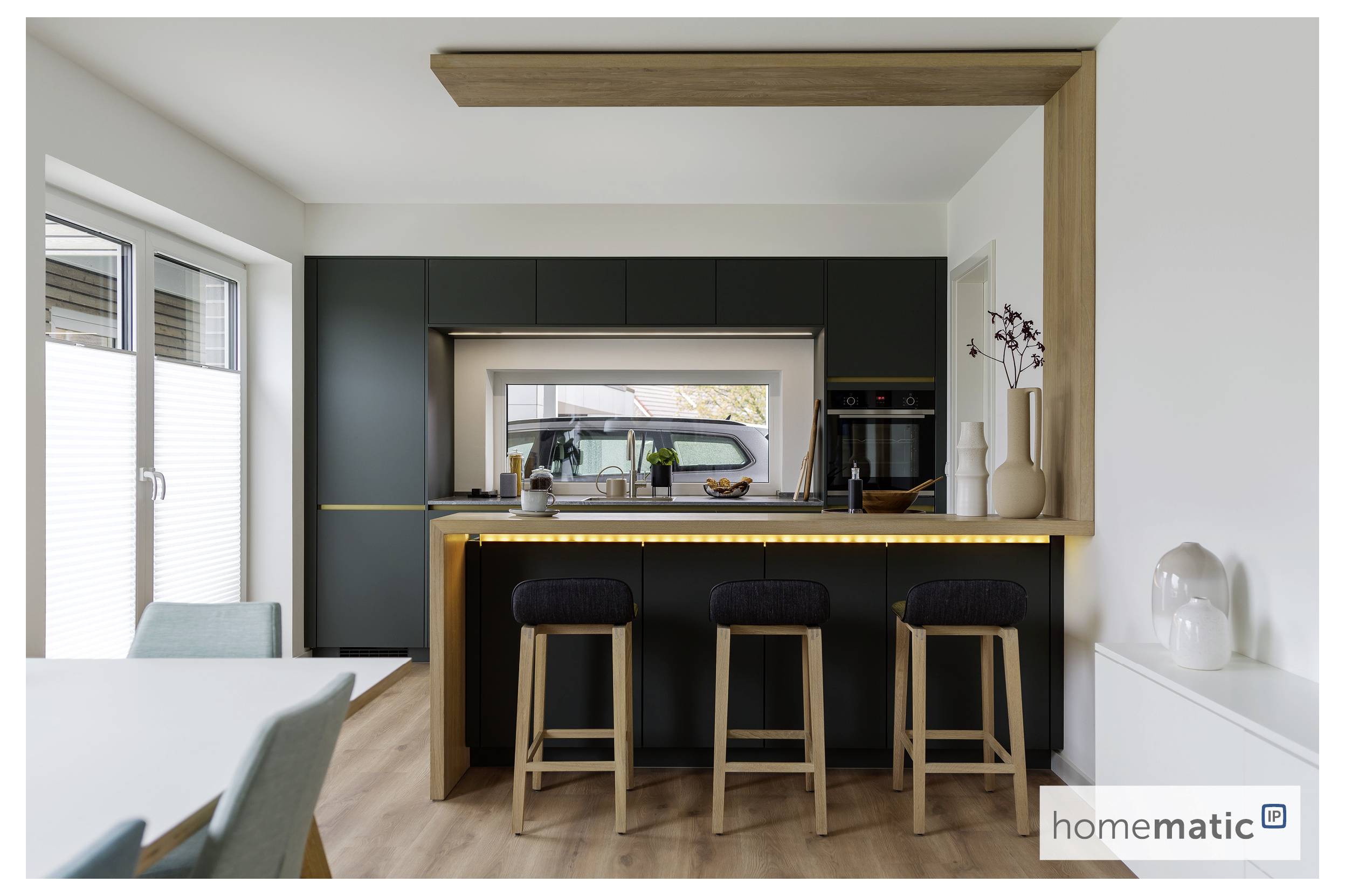 Moderne Küche mit einer dunkelgrauen Insel, Holzhockern und Ambientebeleuchtung. Großes Fenster, weiße Wände und minimalistische Dekoration.