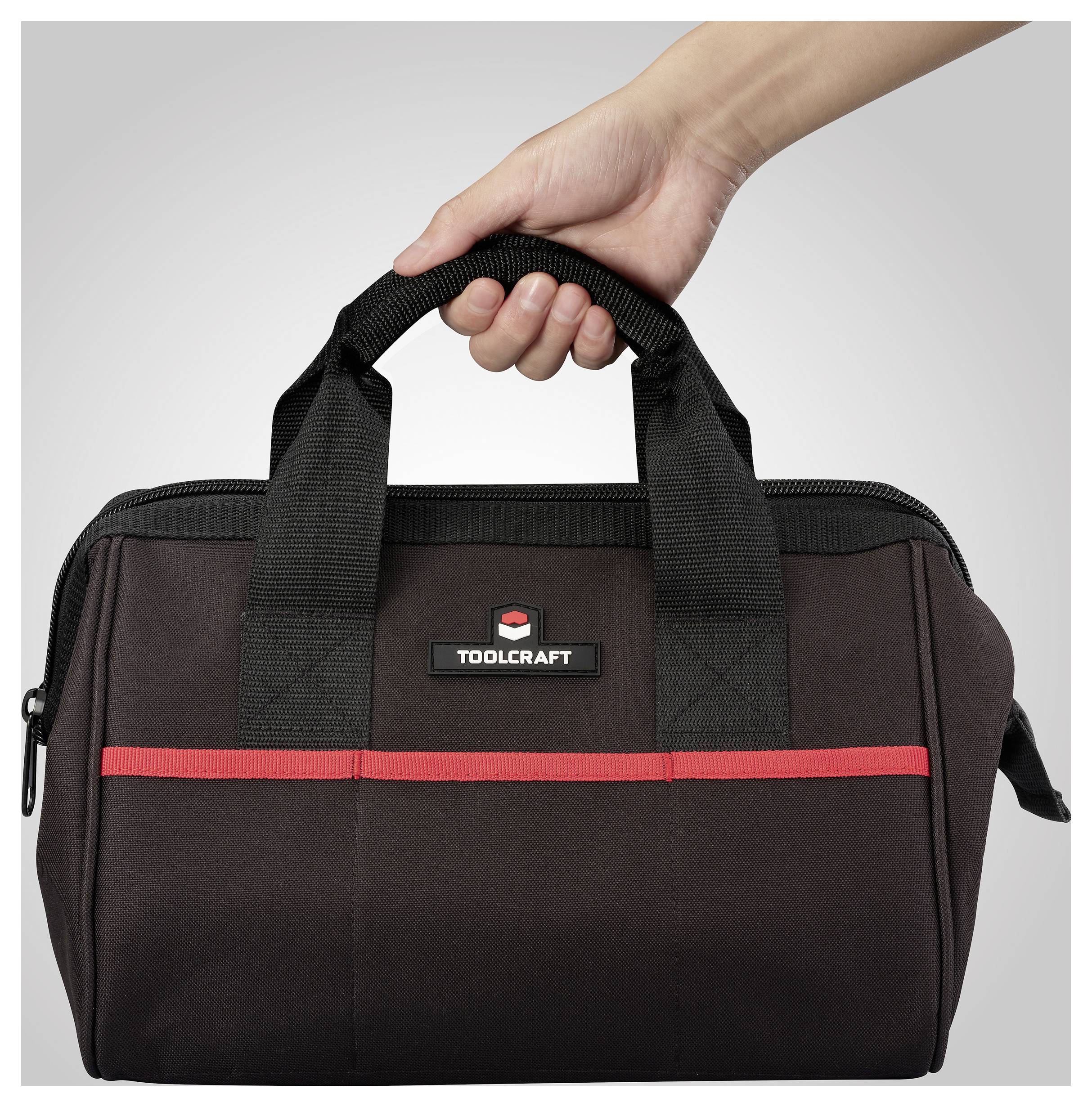 Eine Hand hält eine schwarze und rote Werkzeugtasche mit der Aufschrift „TOOLCRAFT