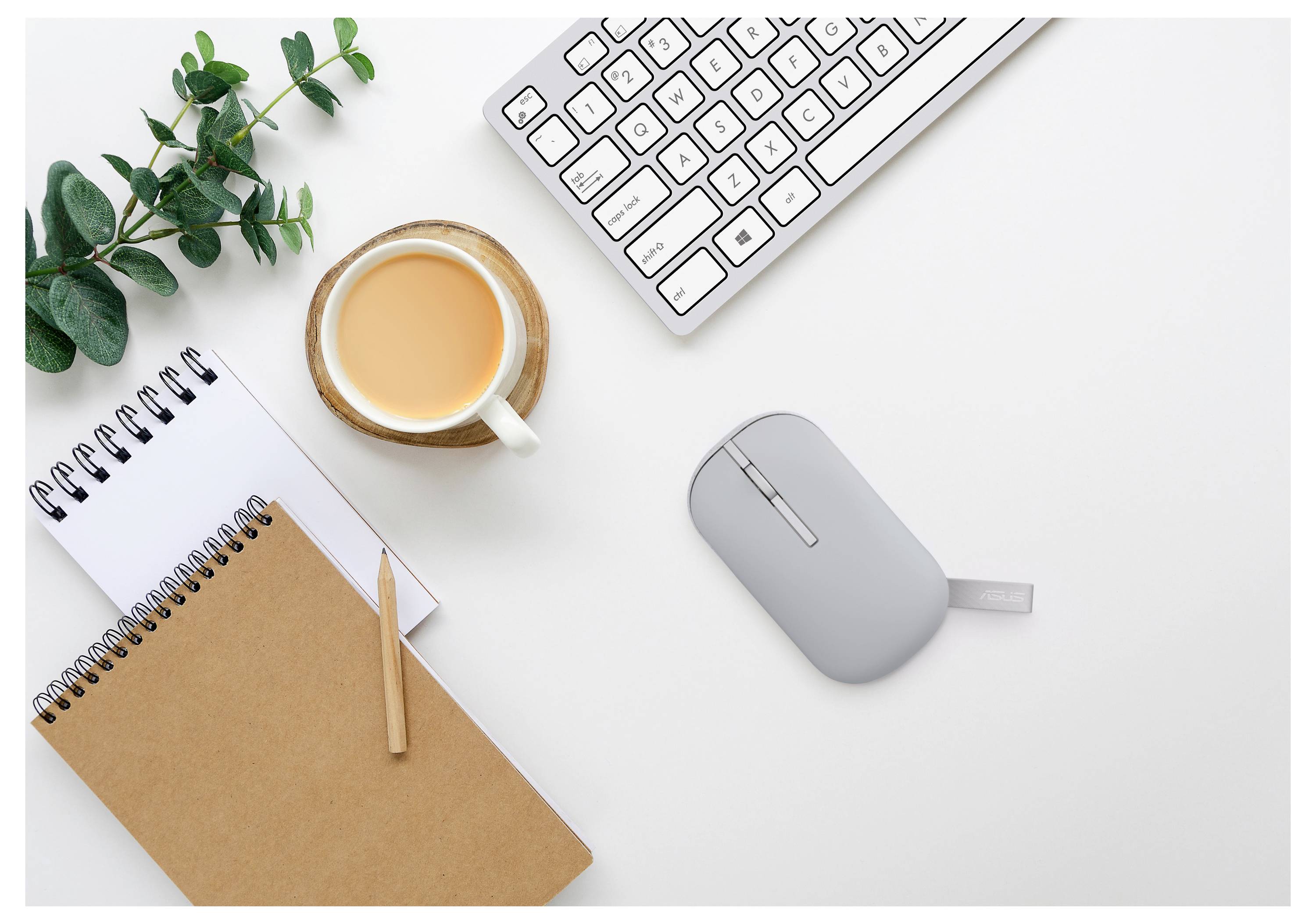 Eine Draufsicht eines minimalistischen Arbeitsplatzes mit einer Tastatur, einer grauen Maus, Notizbüchern, einem Stift und einer Tasse Tee, mit grünen Pflanzenakzenten.