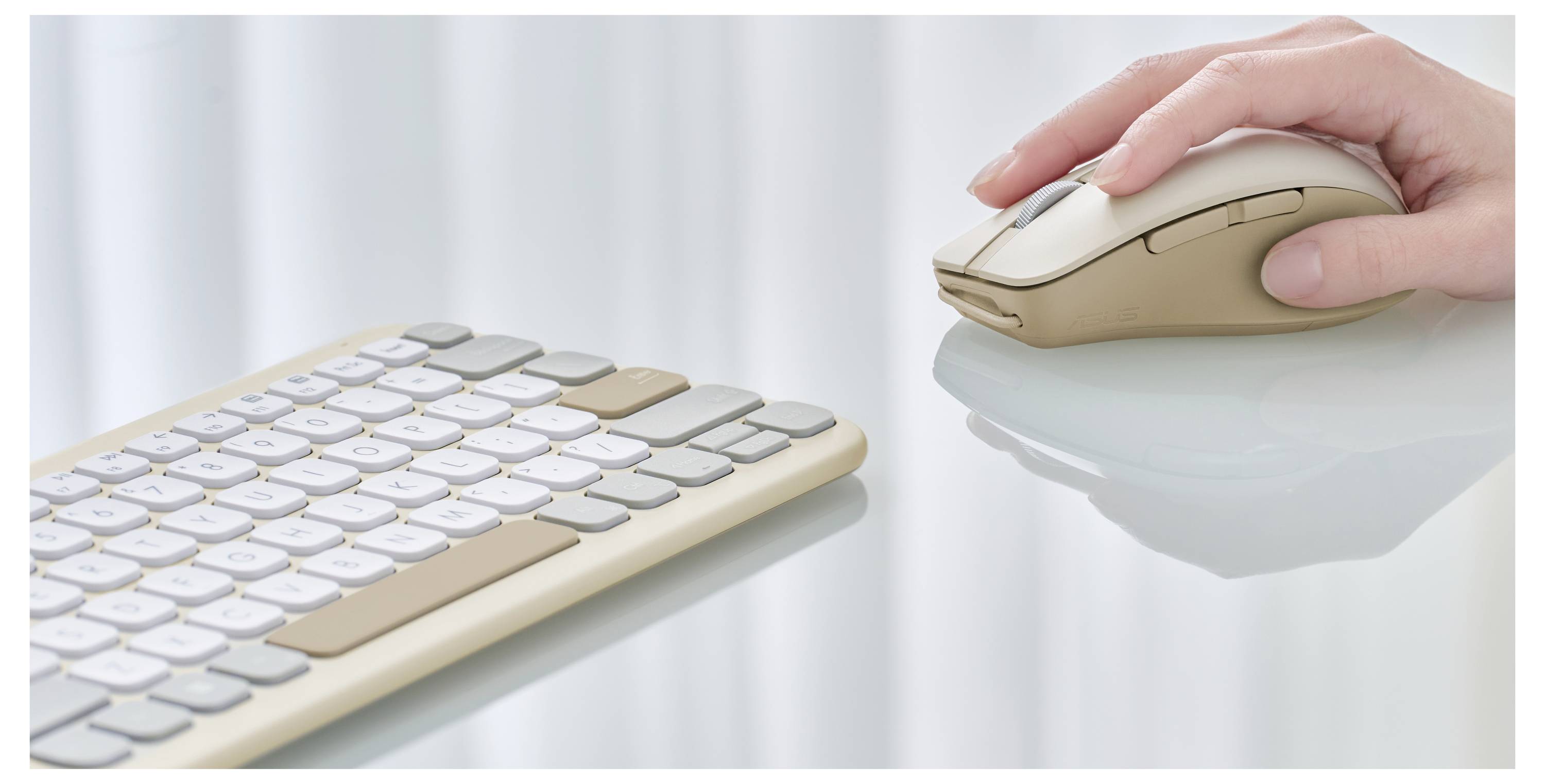 Eine Hand bedient eine beige drahtlose Computermaus neben einer passenden, schlanken Tastatur auf einer reflektierenden Oberfläche.