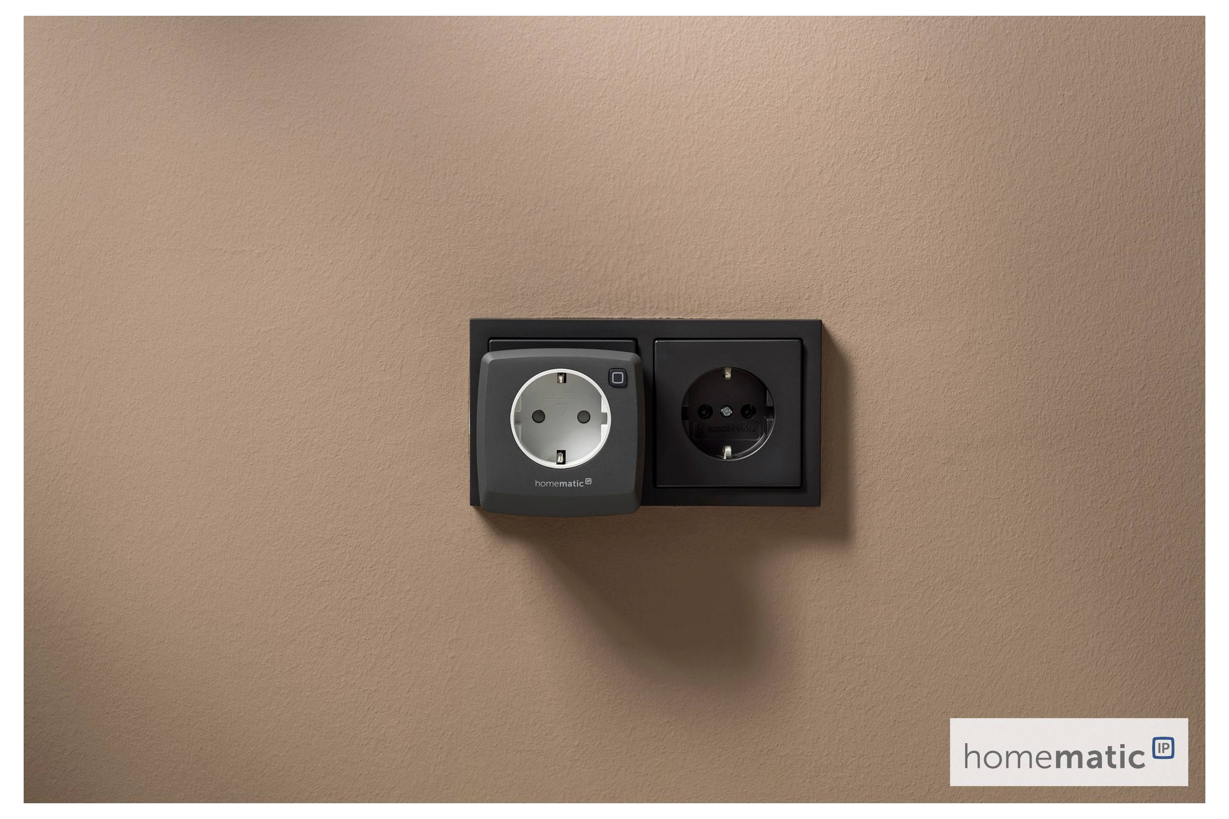 Eine Doppelsteckdose mit einem stylischen intelligenten Steckeradapter an einer beigen Wand, im unteren rechten Ecke mit 'homematic' beschriftet.