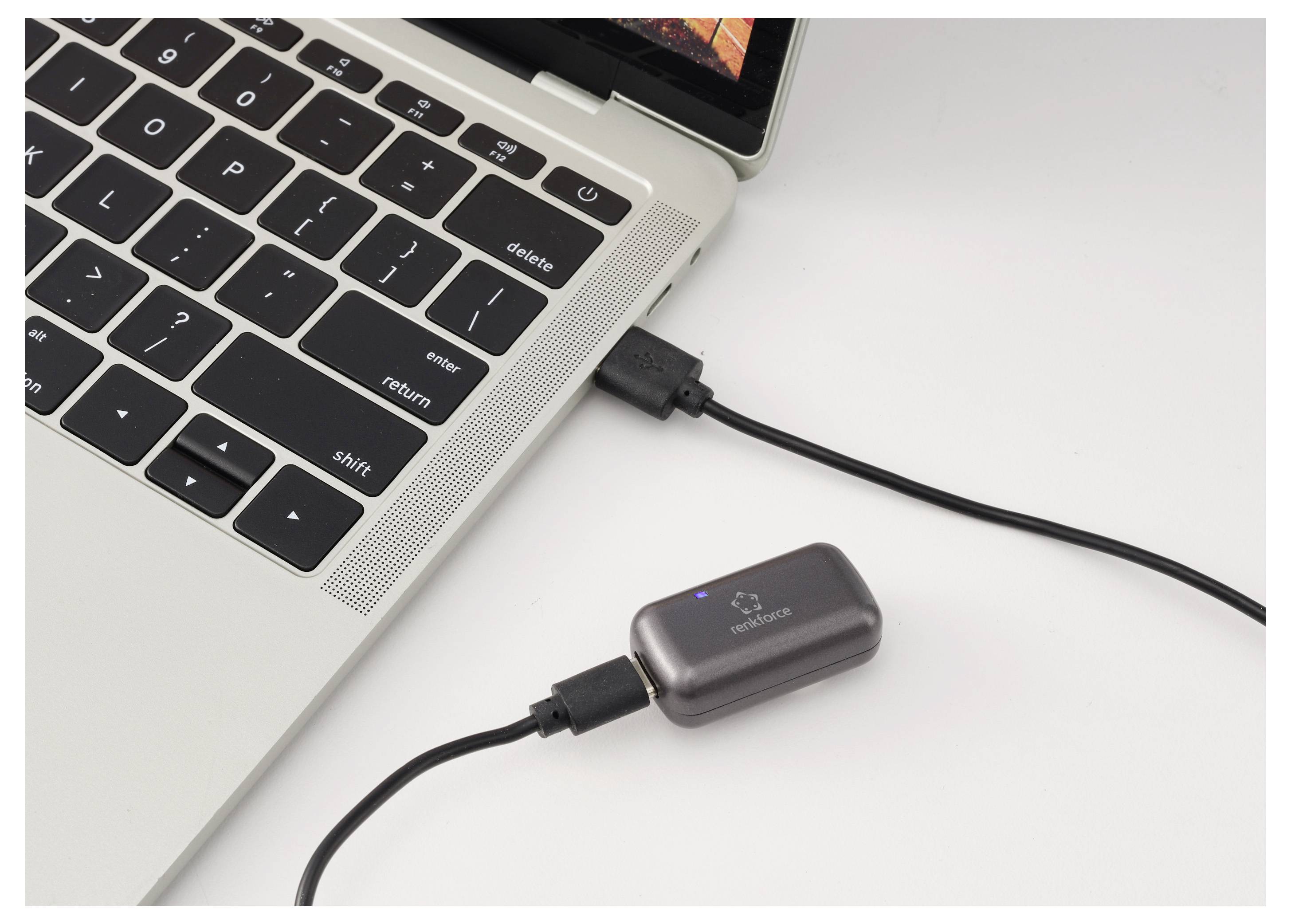 Ein Laptop, der mit einem Kabel mit einem kleinen externen Adapter oder Dongle auf einer weißen Oberfläche verbunden ist.