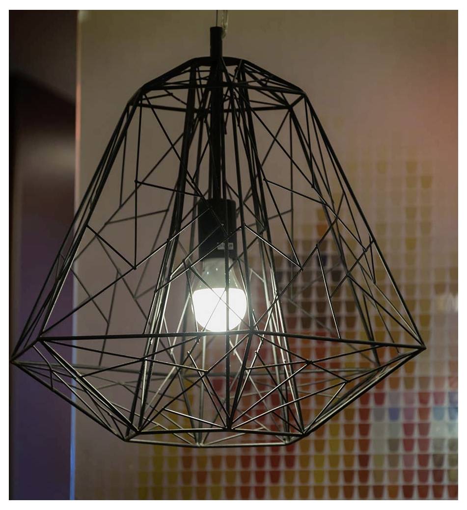 Ein geometrisches Drahtgitter-Lampenschirm umgibt eine brennende Glühbirne und wirft weiches Licht. Der Hintergrund ist ein verschwommenes Mosaik aus weichen Farben.