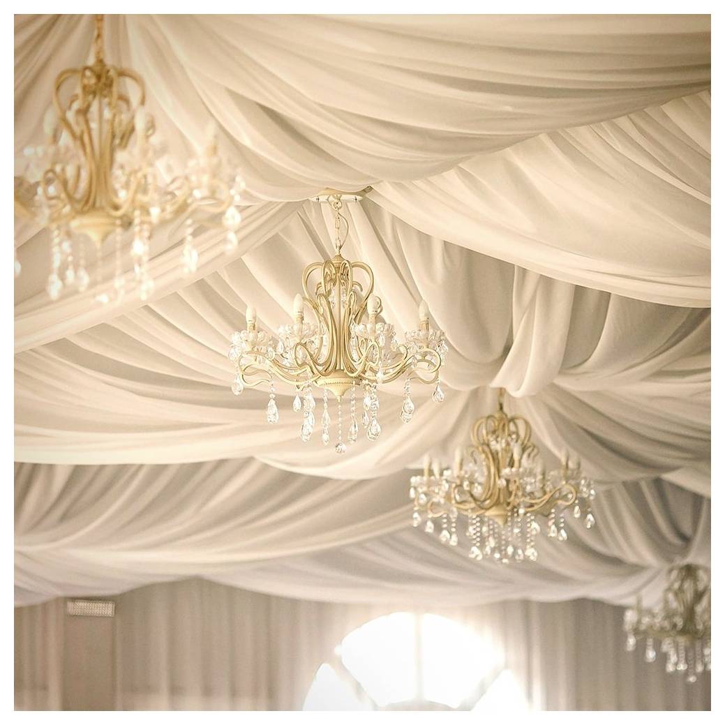 Elegante Decke, verhüllt mit weißem Stoff und geschmückt mit kunstvollen, goldenen Kronleuchtern, die mit herabfallenden Kristallakzenten versehen sind.