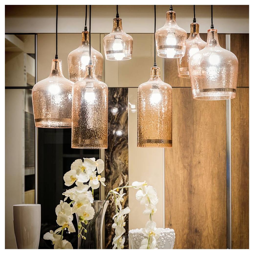 Pendelleuchten mit großen Glasschirmen in einem warmen Bronzeton hängen über einem modernen Innenraum. Weiße Orchideen in einer Vase verleihen darunter Eleganz.