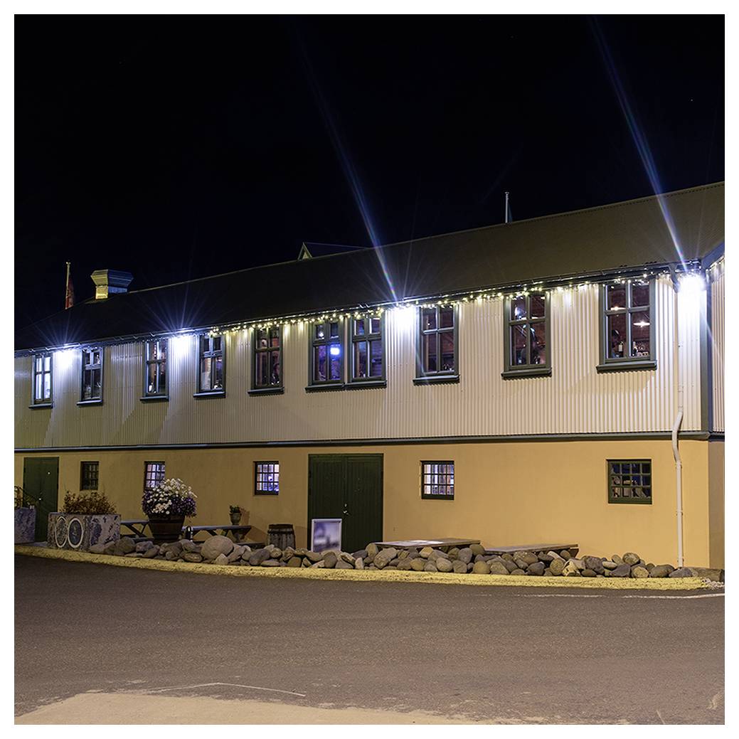 Ein langer Gebäude bei Nacht, beleuchtet von Außenbeleuchtung mit mehreren Fenstern und einem mit Steinen gesäumten Weg im Vordergrund.