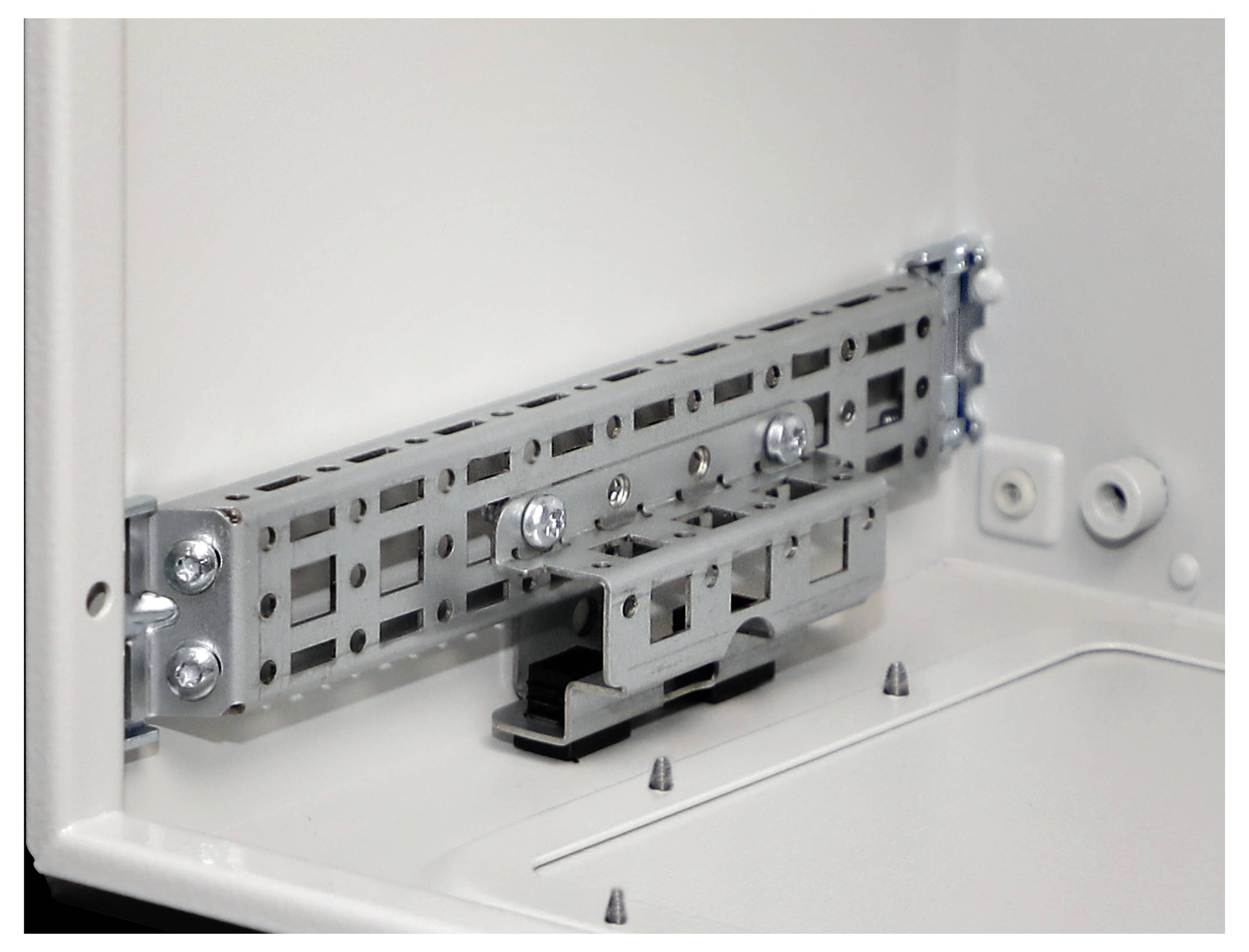 Ein Schaltschrank-Innenraum, der einen metallfarbenen Montagebügel zeigt, der mit Schrauben befestigt ist. Der Schaltschrank ist geöffnet und gibt seine Struktur preis.