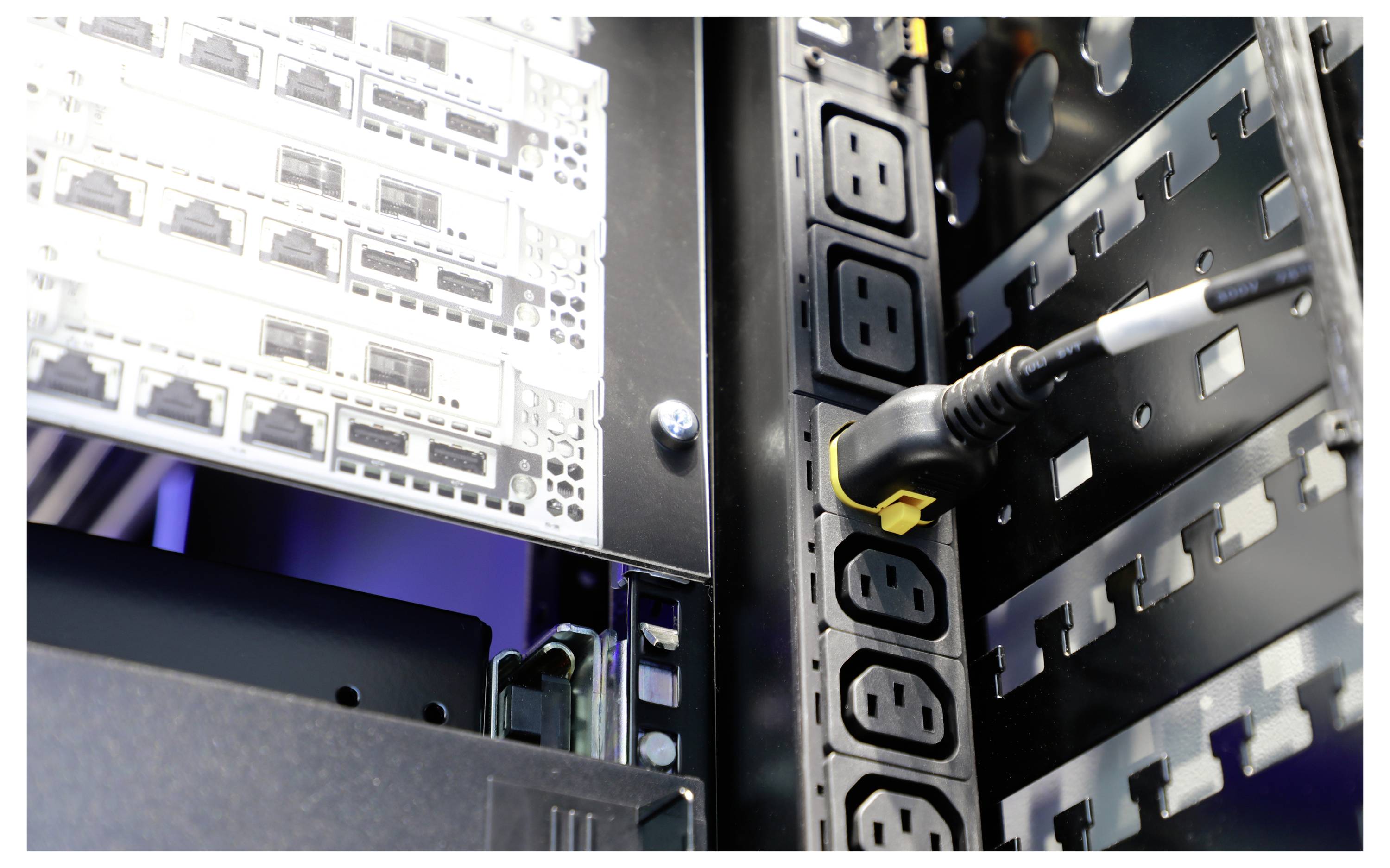 Nahaufnahme eines Serverracks, das Netzwerkausrüstung und Netzkabel zeigt und die Konnektivität und Energiemanagement in einem Rechenzentrum hervorhebt.