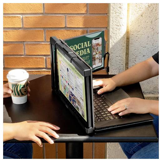 Zwei Personen sitzen an einem Tisch; eine von ihnen benutzt einen Laptop mit einem Dual-Screen-Erweiterungsdisplay, auf dem eine farbenfrohe Webseite geöffnet ist. Eine Kaffeetasse steht auf dem Tisch.