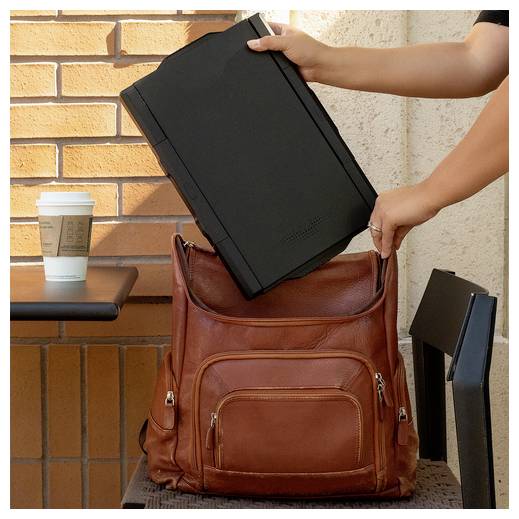 Eine Person legt einen schwarzen Laptop in einen braunen Lederrucksack auf einen Stuhl. Ein Tisch mit einer Kaffeetasse aus einem Café steht in der Nähe.