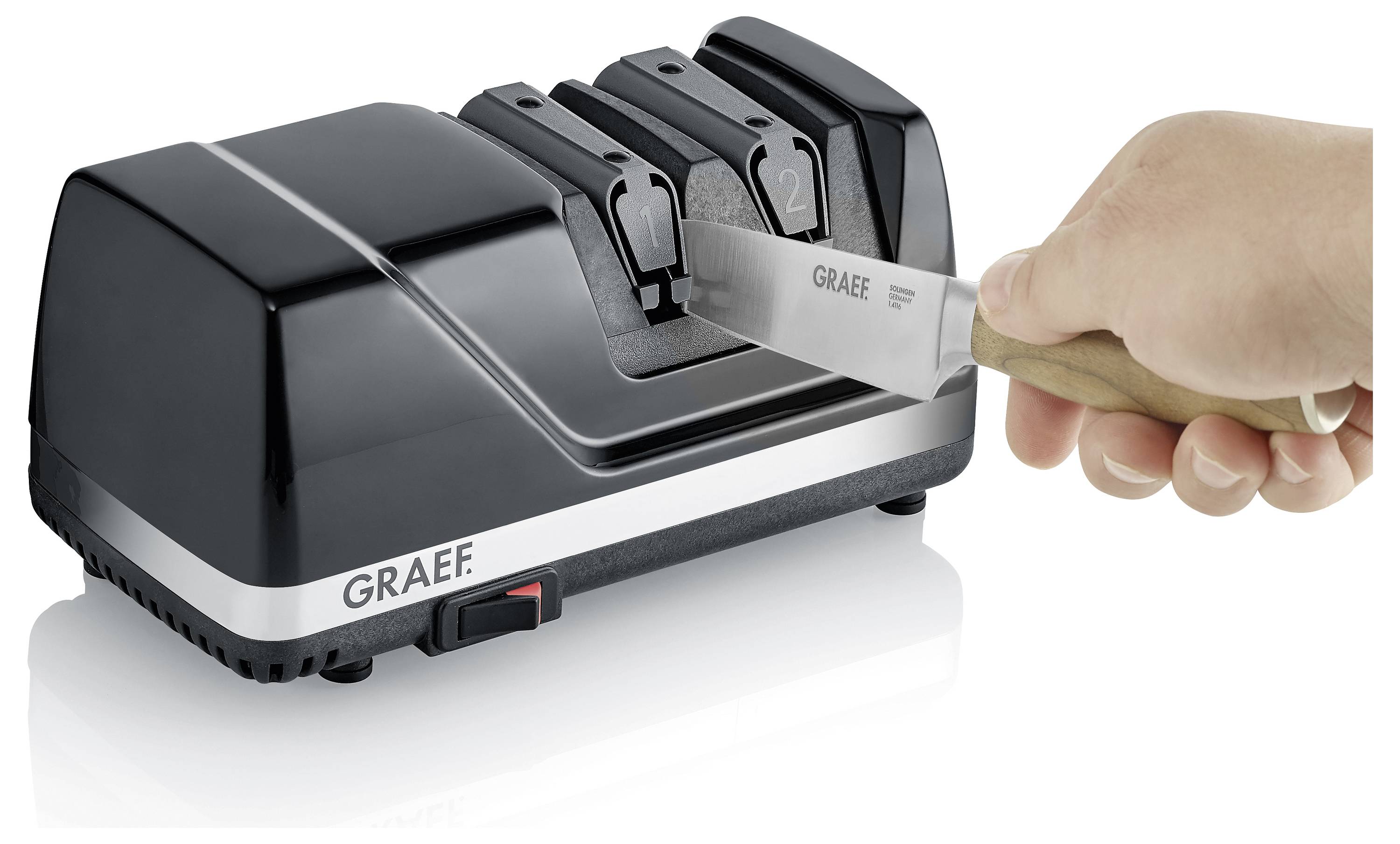 Eine Hand schärft ein Messer mit einem schwarzen Graef elektrischen Messerschärfer, der zwei mit '1' und '2' nummerierte Schlitze aufweist.