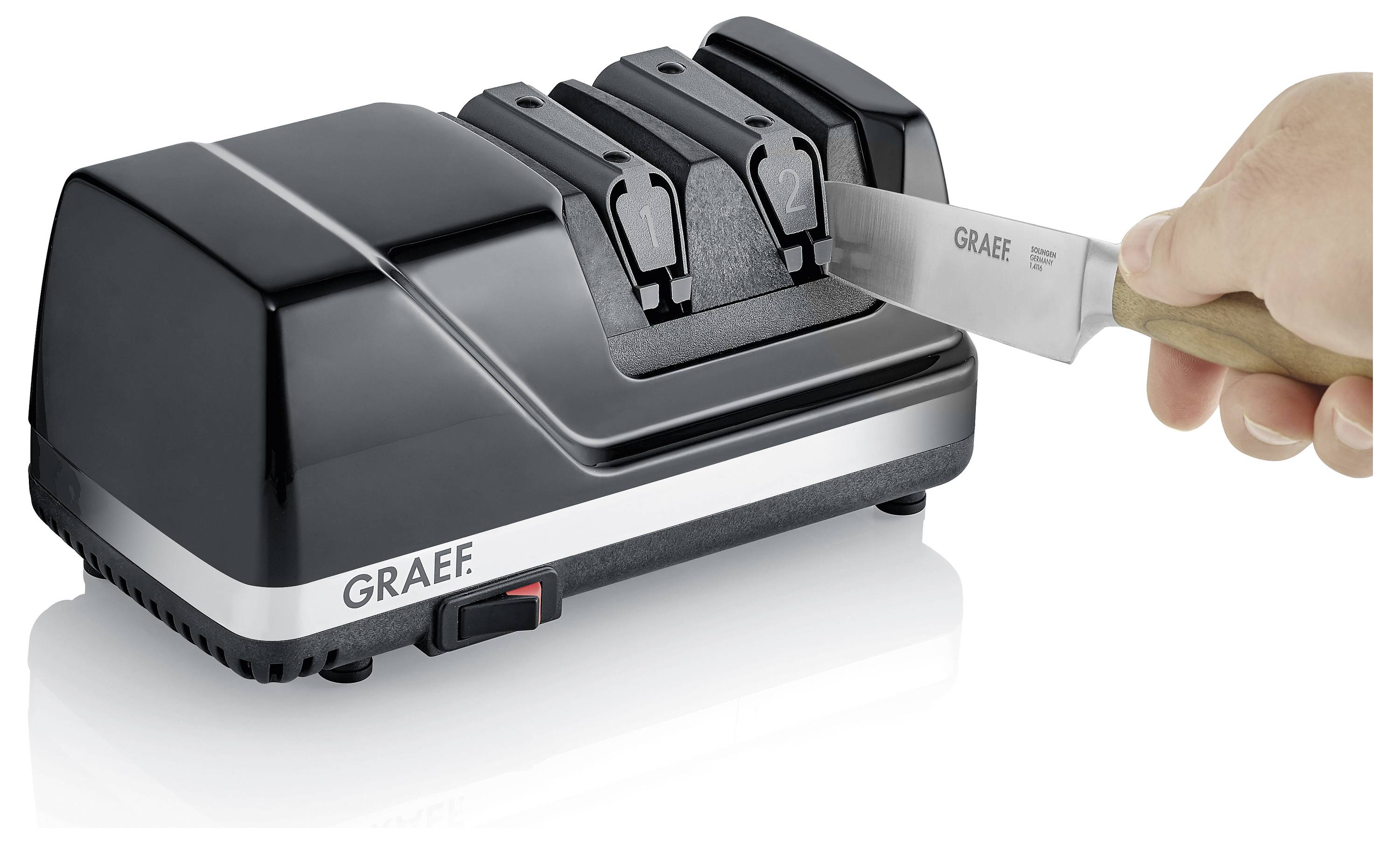 Eine Person schärft ein Messer mit einem schwarzen elektrischen Messerschärfer, der zwei Stufen mit den Bezeichnungen „1