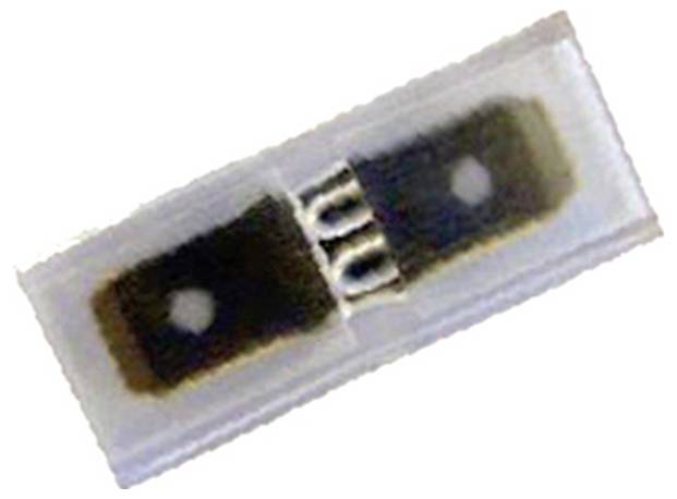 Eine kleine, transparente Kunststoffkomponente mit dunklen Abschnitten und Metallkontakten, möglicherweise ein Mikrochip oder elektronisches Bauteil, von oben betrachtet.