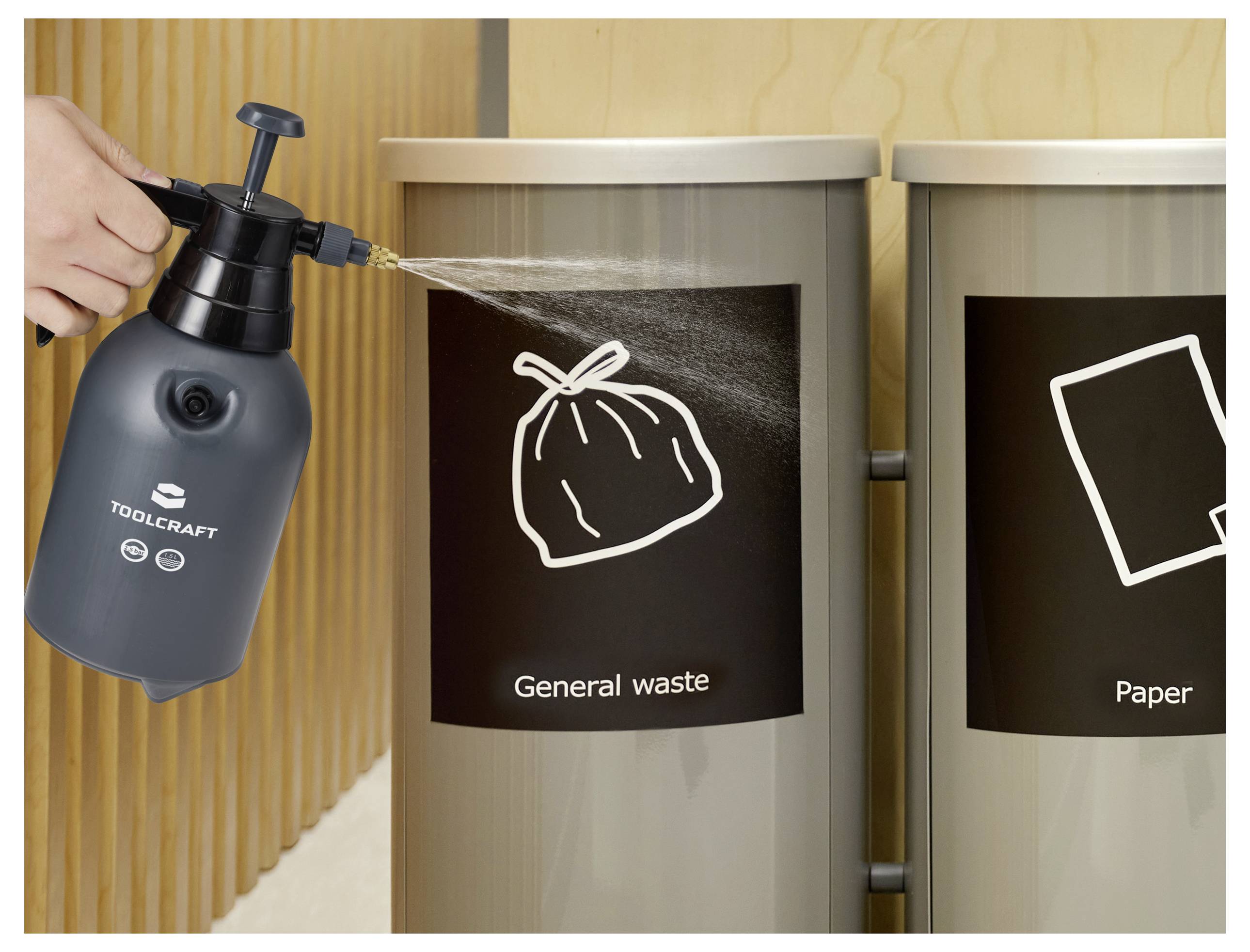 Eine Person sprüht ein Behältnis für Allgemeinen Müll, das mit einem Müllsack-Symbol gekennzeichnet ist, neben einem Papierrecycling-Behältnis.