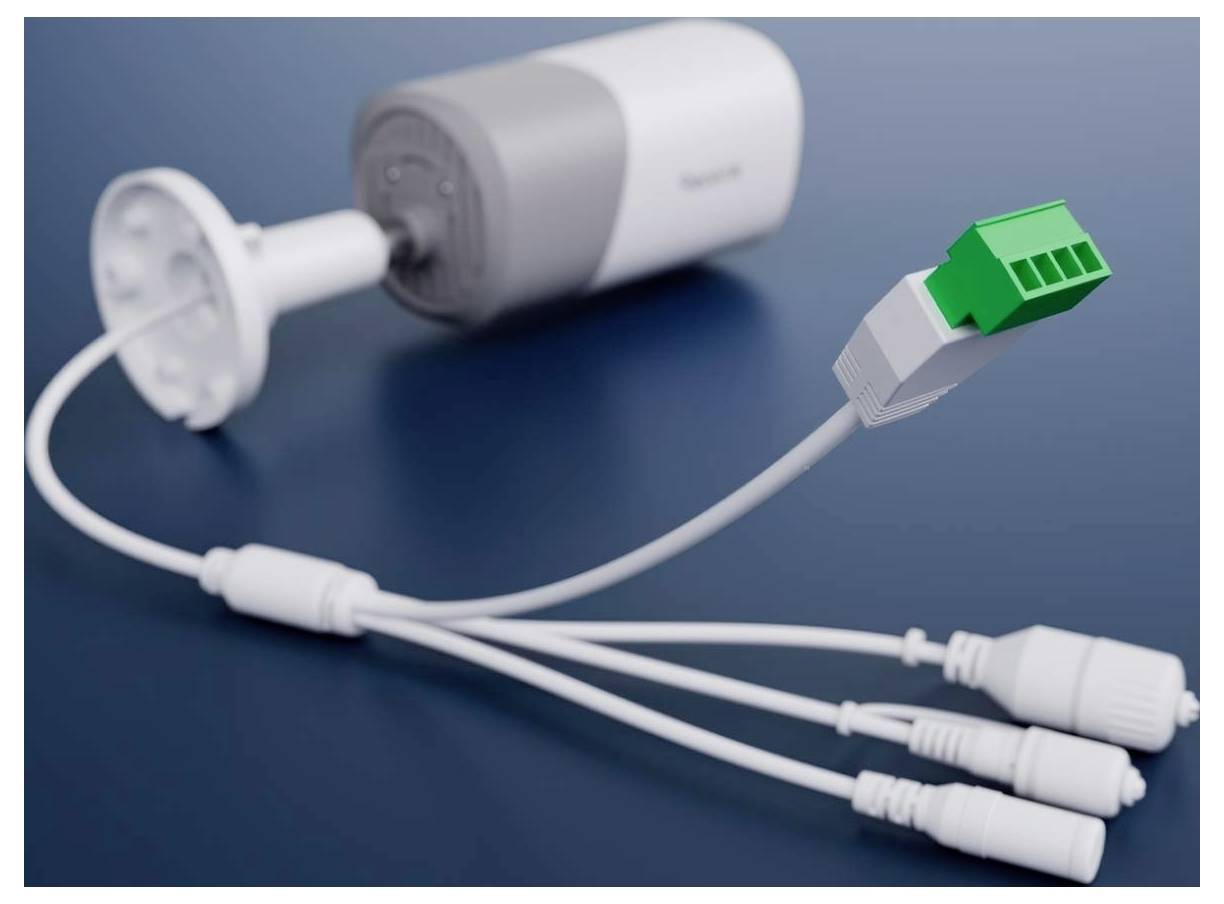 Eine Sicherheitskamera mit mehreren Anschlüssen, einschließlich eines grünen Terminalblocksteckers, befindet sich auf einer blauen Oberfläche.