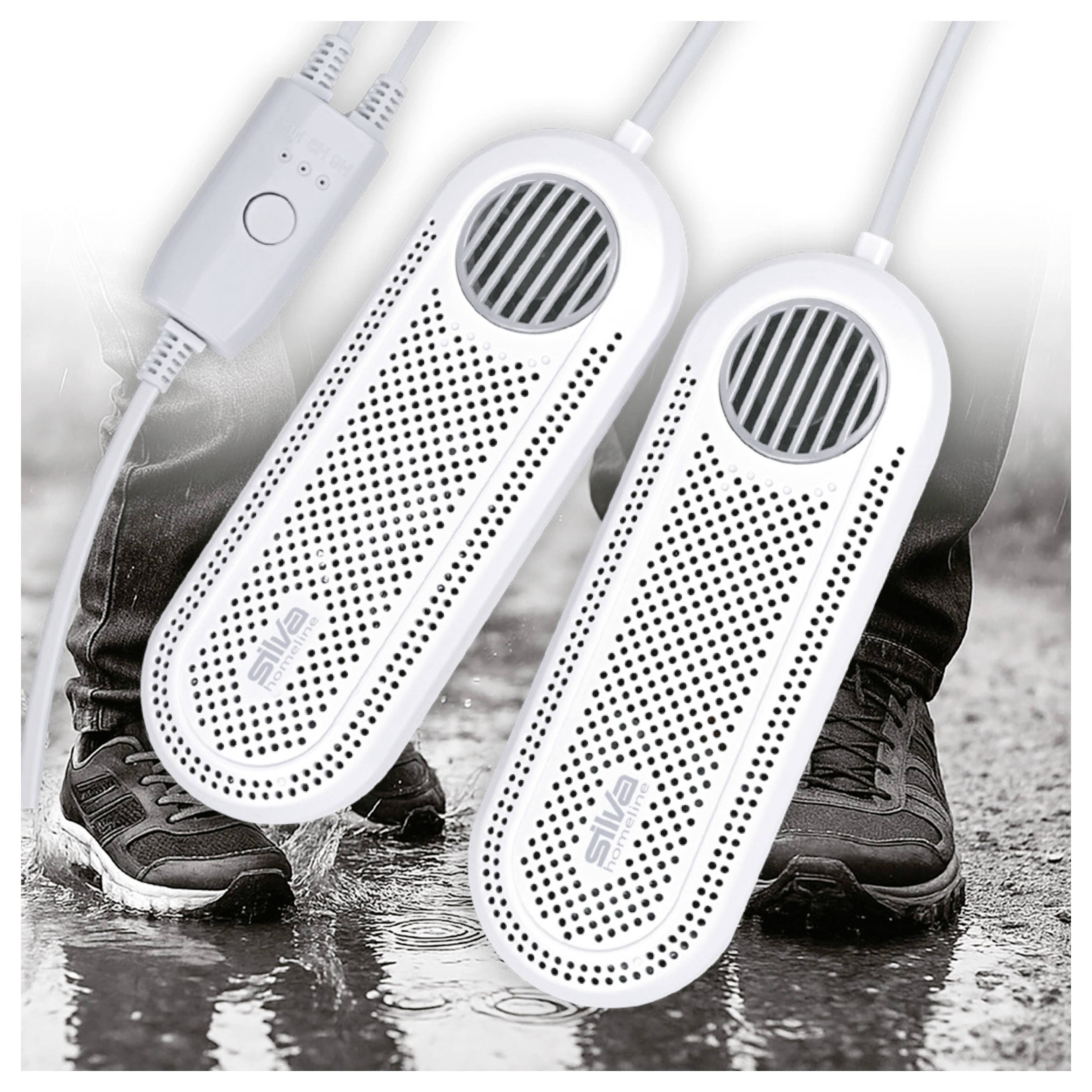 Zwei weiße Schuhtrockner, jeweils mit Belüftungsöffnungen und Kabeln, auf einer feuchten Oberfläche platziert. Beine in schwarzer Hose und Schuhen sind im Hintergrund zu sehen.