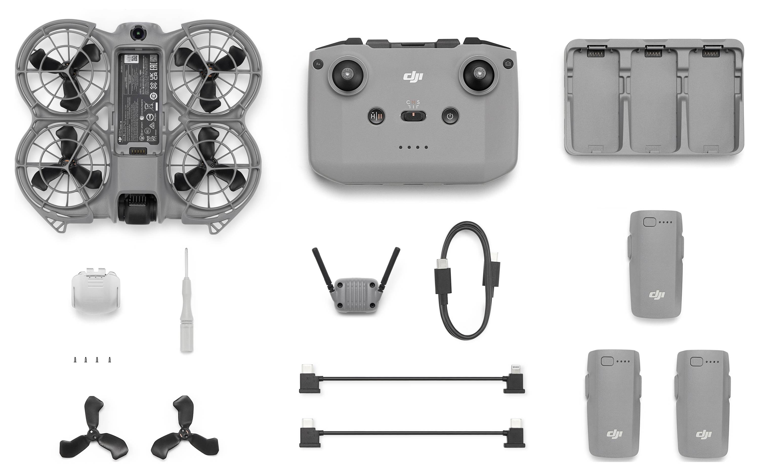 Ein kompaktes Drohnen-Set bestehend aus einer kleinen Drohne, Fernbedienung, zwei Akkus, Propellern, einem Ladehub und Anschlüssen vor weißem Hintergrund.