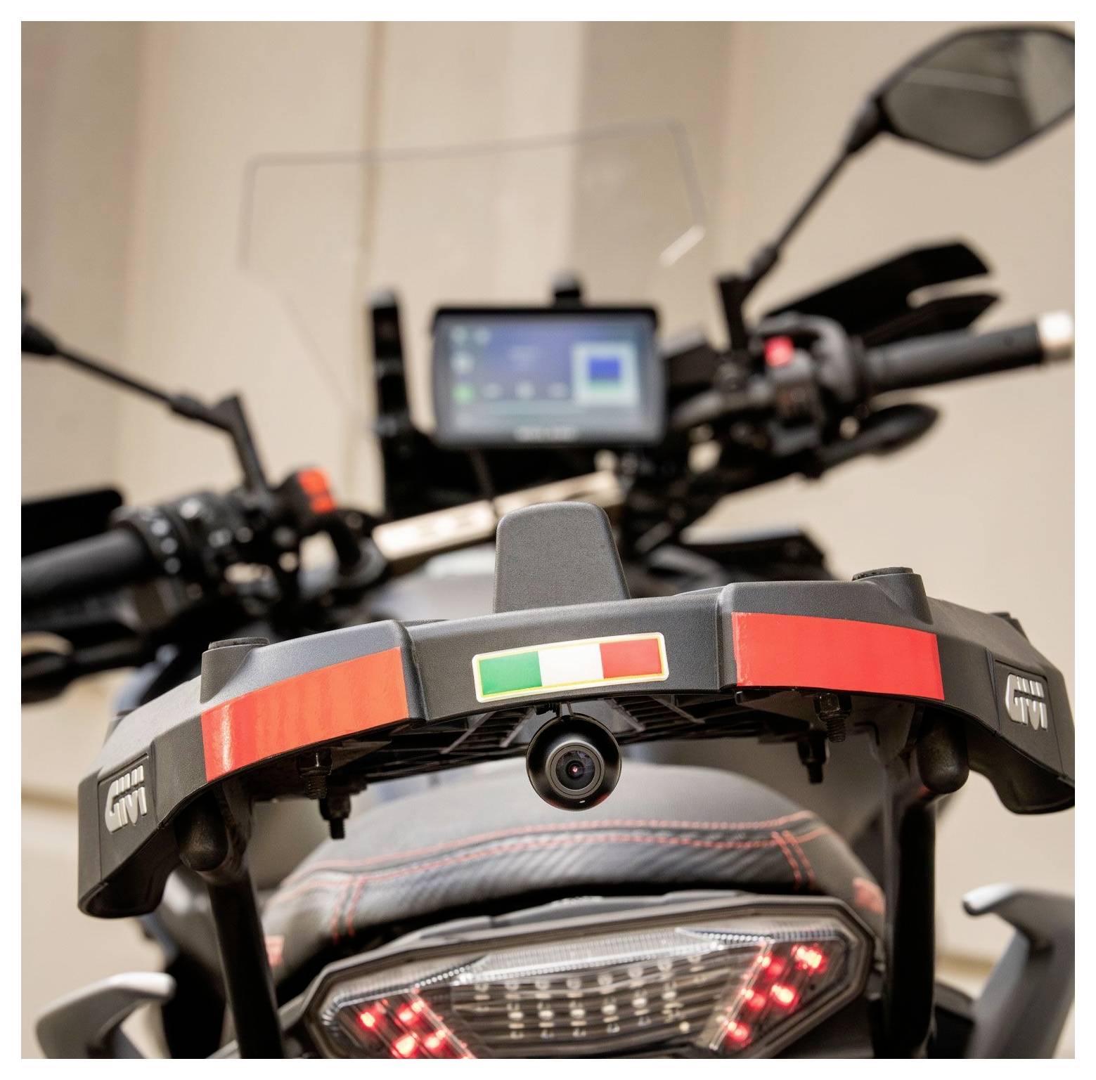 Rückansicht eines Motorrads mit einem Aufkleber der italienischen Flagge auf einem Topcase-Halter, ausgestattet mit einem digitalen Anzeigebildschirm und einem Kennzeichenhalter.