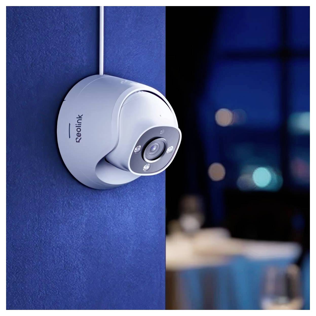 Eine Sicherheitskamera, montiert an einer blauen Wand, gerichtet auf einen dunkel beleuchteten Raum mit verschwommenen Lichtern im Hintergrund.