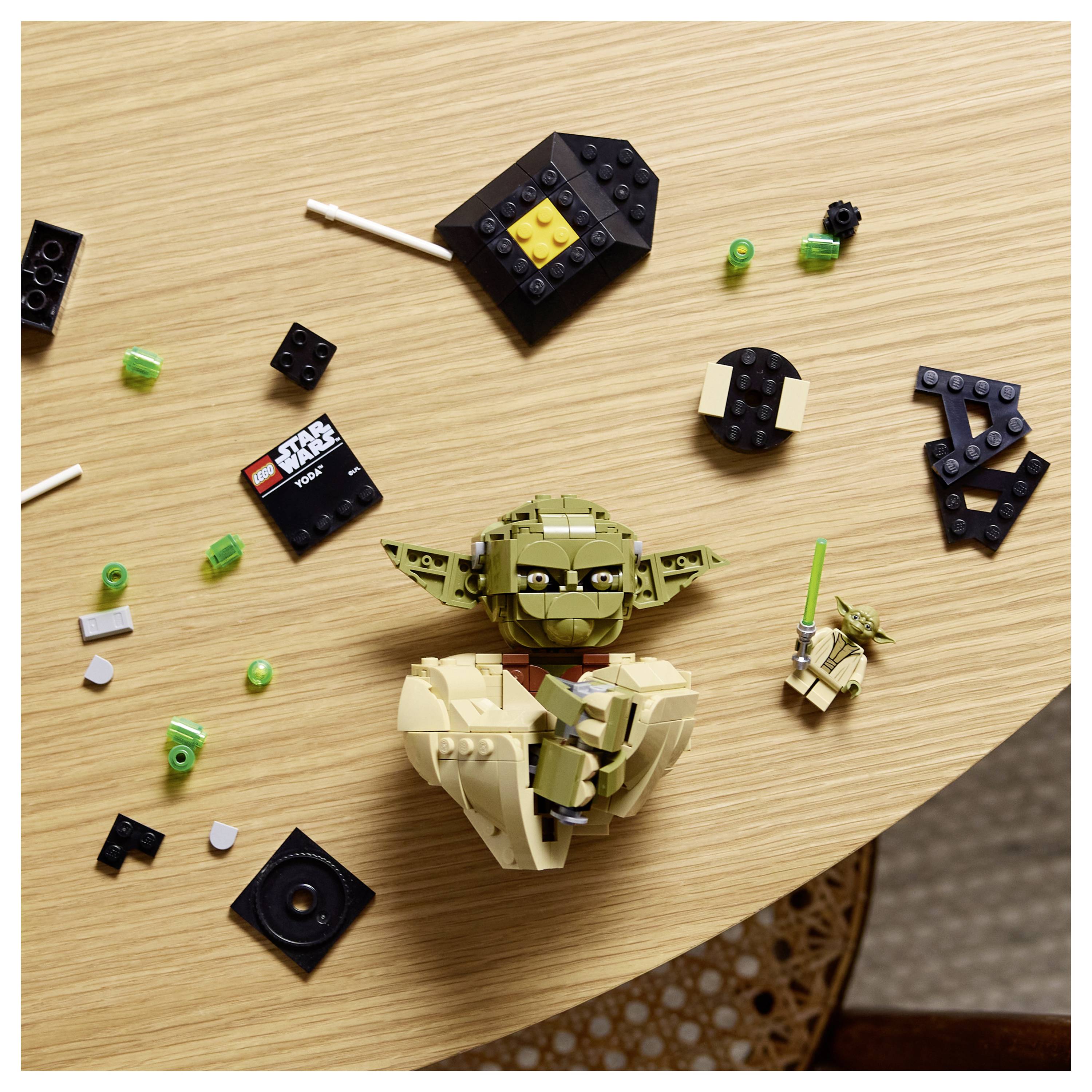 LEGO-Yoda-Figur, teilweise zusammengebaut auf einem Holztisch, umgeben von verstreuten LEGO-Steinen und einer Mini-LEGO-Yoda-Figur mit einem Lichtschwert.