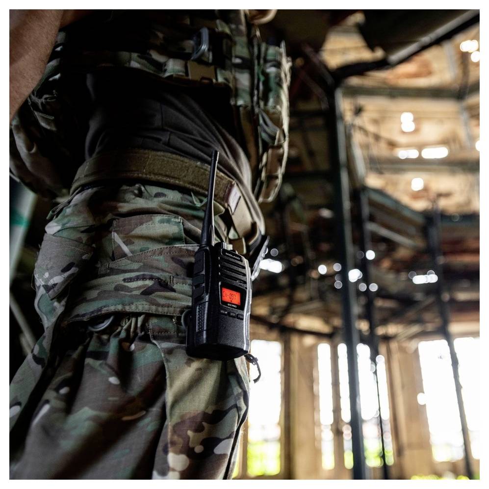 Ein Soldat in Tarnuniform steht in einem verfallenen Gebäude. Ein Funkgerät ist an seinem Gürtel befestigt.