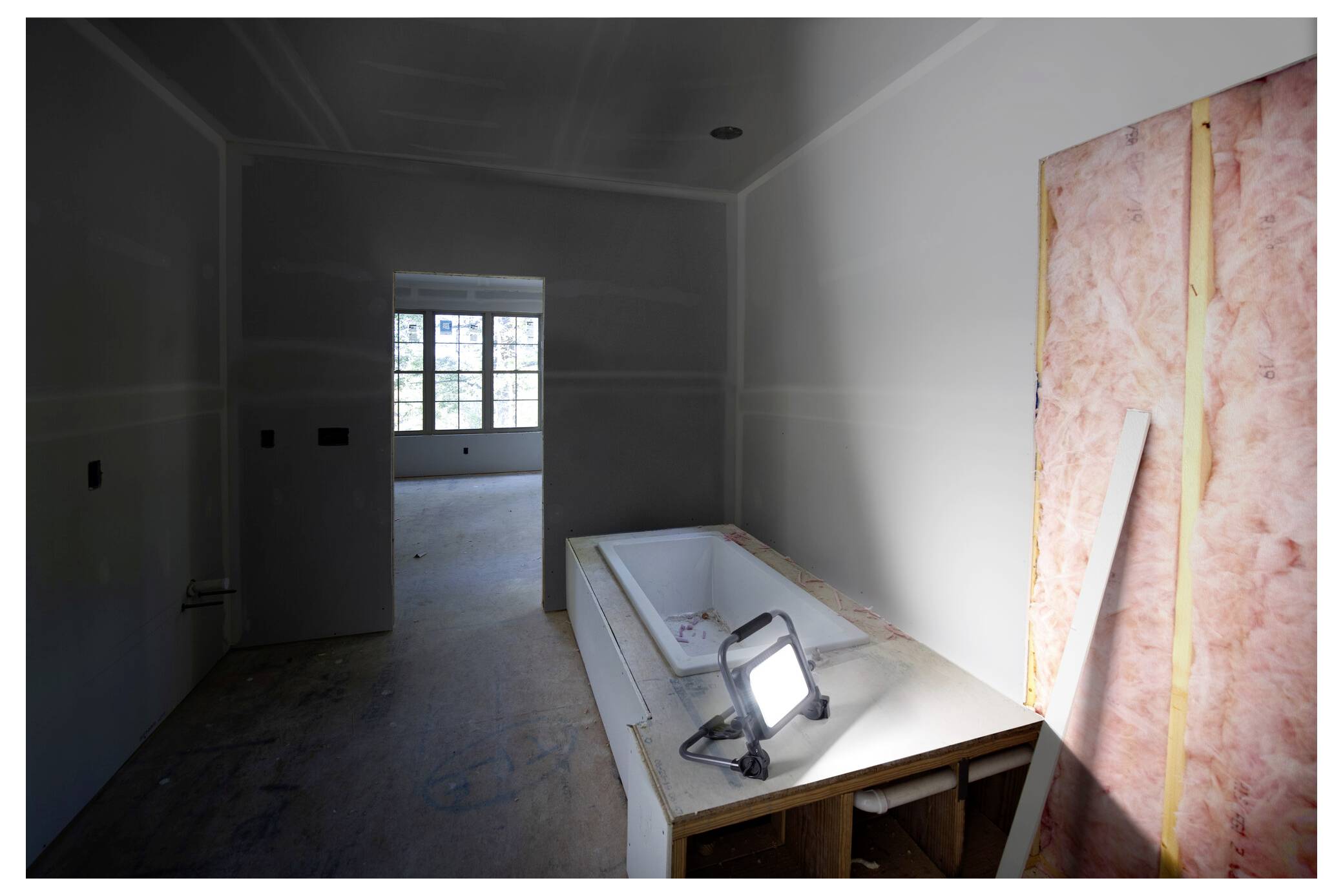 Ein Raum im Bau mit kahlen Wänden und Böden, mit einer teilweise montierten Badewanne und einer Arbeitslampe, die Licht wirft.