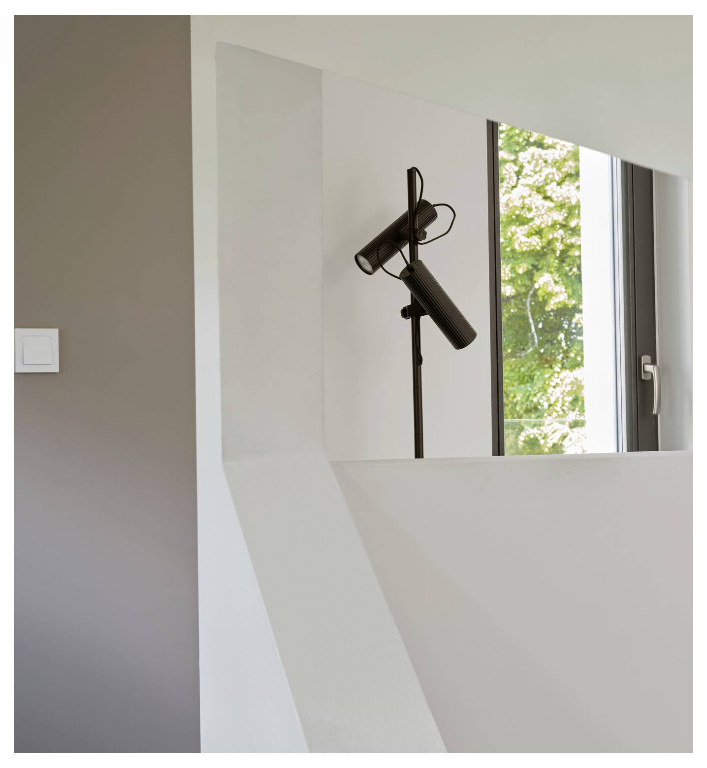 Ein schwarzes Mikrofon auf einem Ständer in einem minimalistischen Raum mit neutralen Wänden und einem großen Fenster, das einen Blick auf Grünflächen nach draußen bietet.